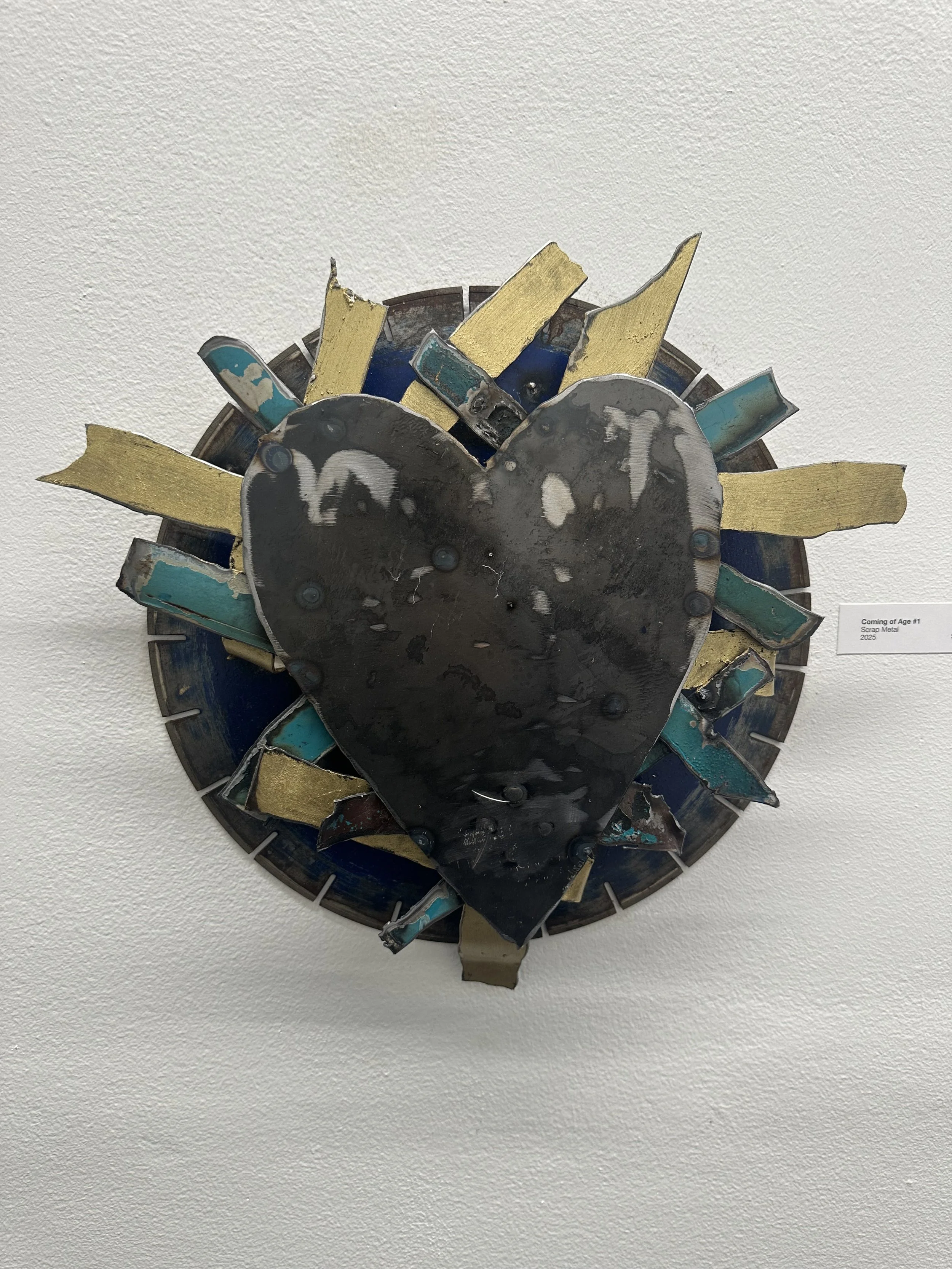 Mixed metal sculpture of a heart surrounded by an array of metal pieces and a circular metal frame.