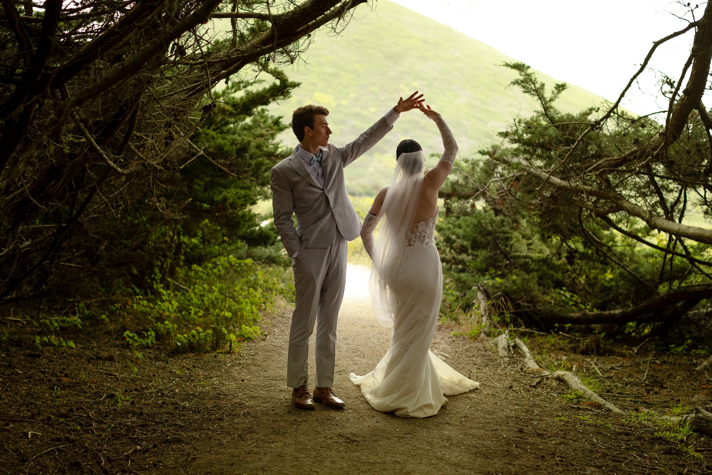 A bride and groom dancing together on a forest trail with greenery and trees surrounding them.