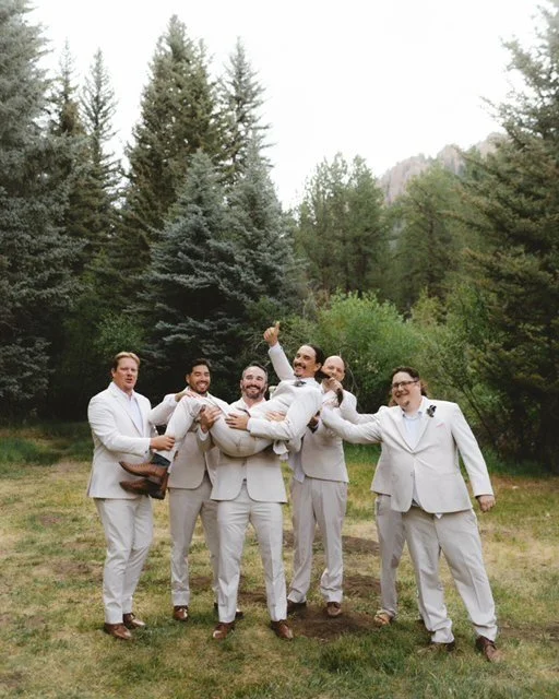 Groom lifting his groomsmen outdoors surrounded by trees.