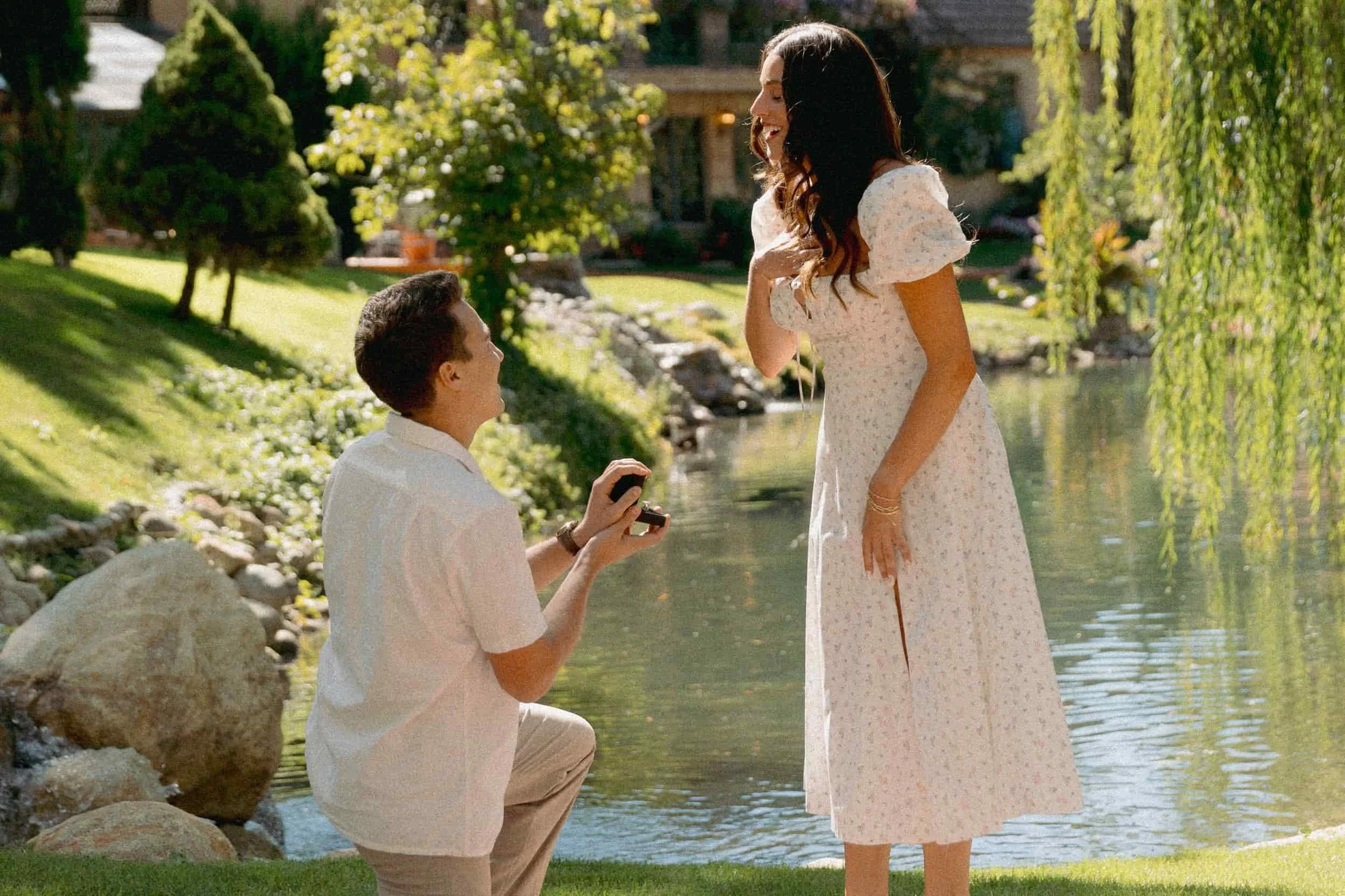 Surprise proposal at La Caille in Utah with Tom kneeling by the water as Natalie reacts, a real Utah proposal ideas moment