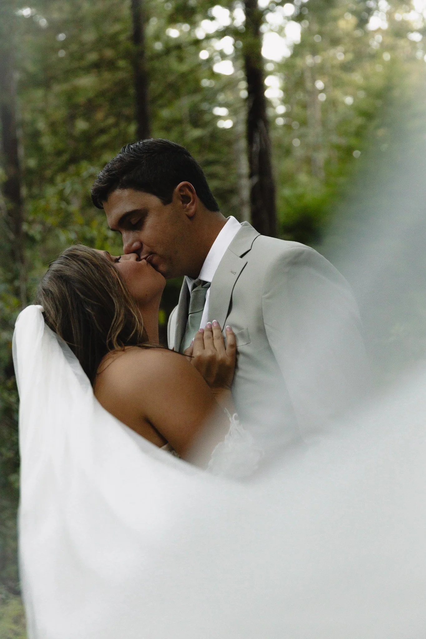 A bride and groom kissing in a forest setting during their wedding ceremony.
