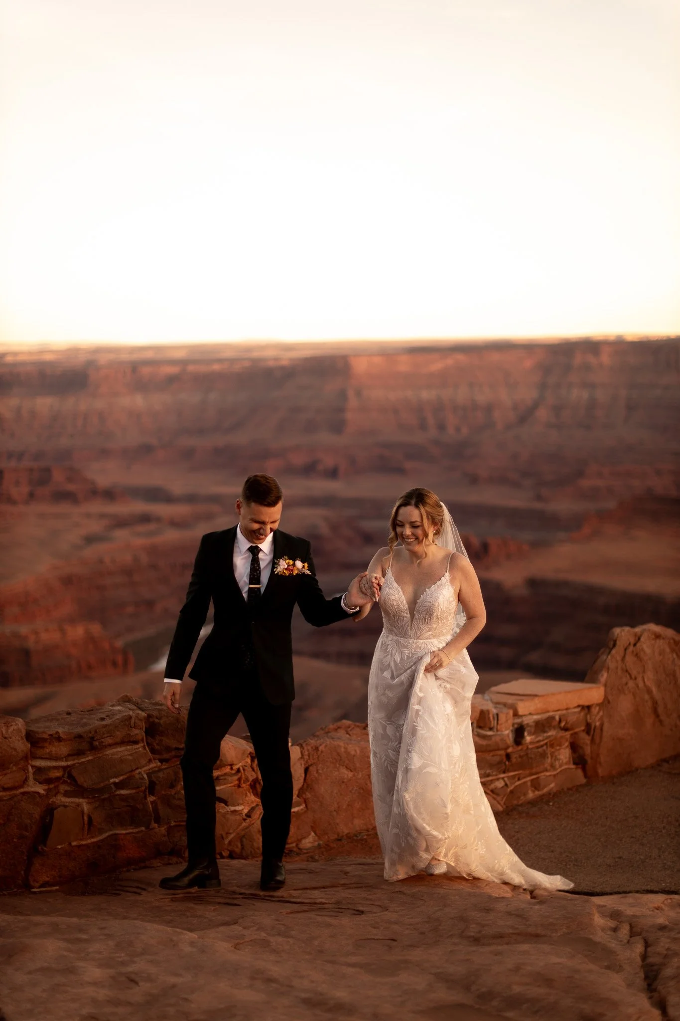 A bride and groom holding hands and walking at the Grand Canyon during sunset.