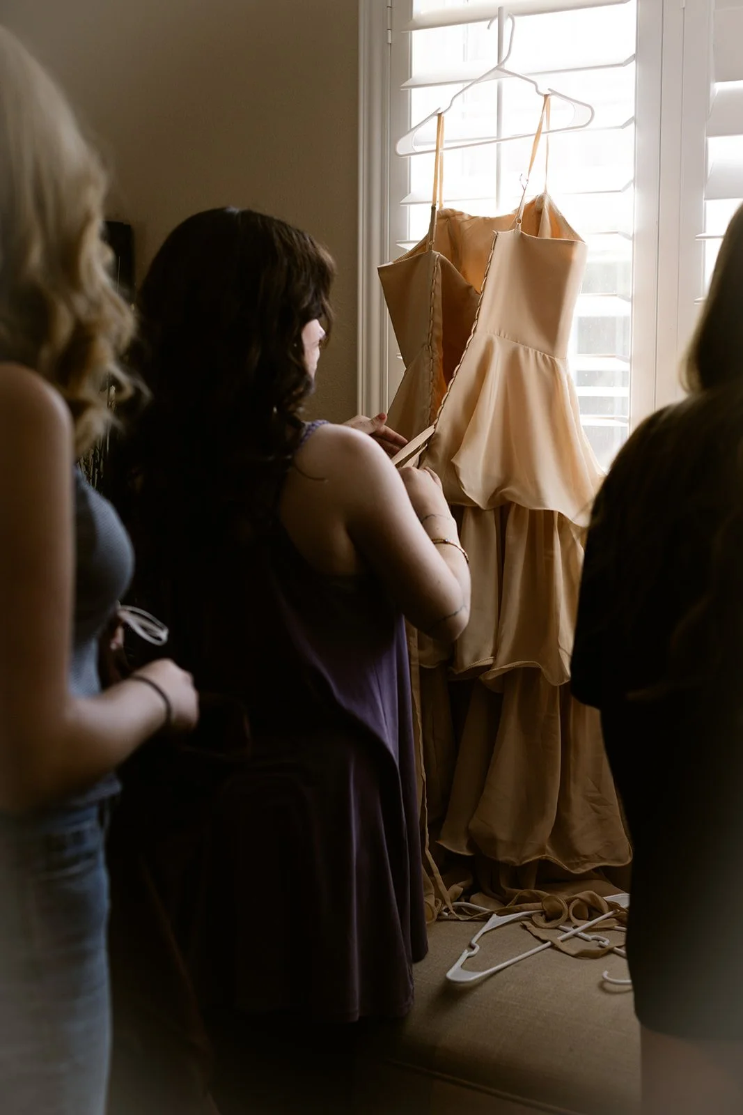 Women looking at beige dresses hanging by the window.