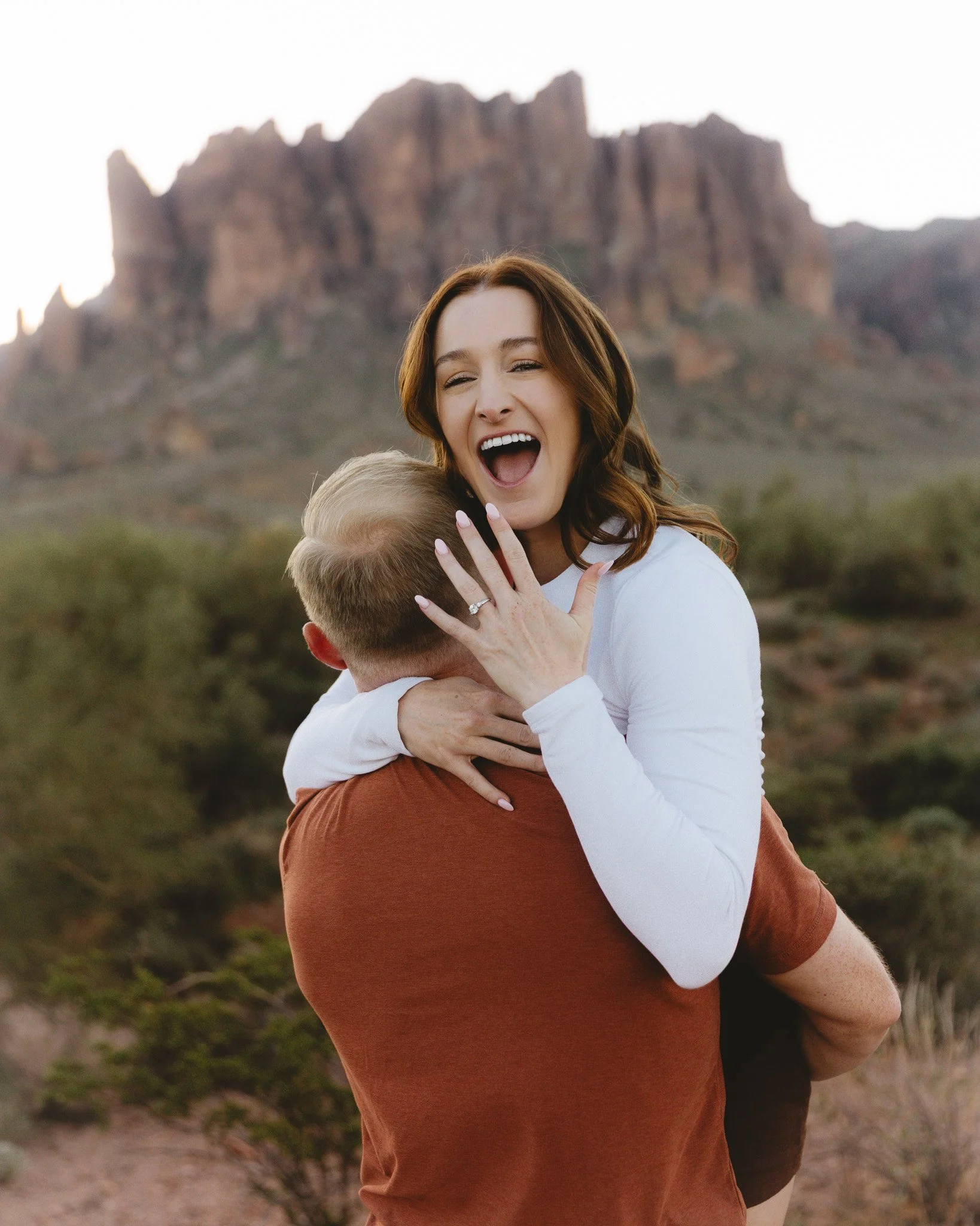 A woman hugging a child outdoors with mountains in the background.