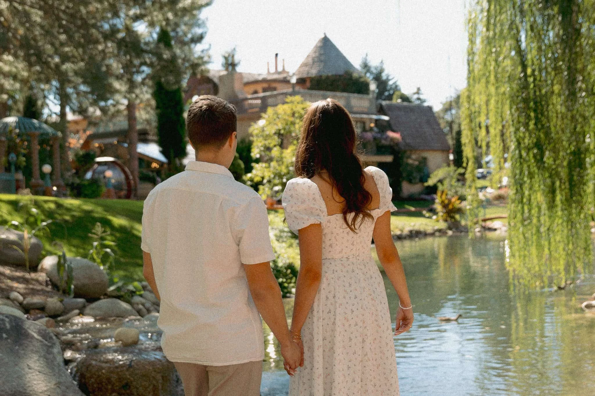 Natalie and Tom walking through La Caille gardens in Utah with scenic pond and mountain backdrop