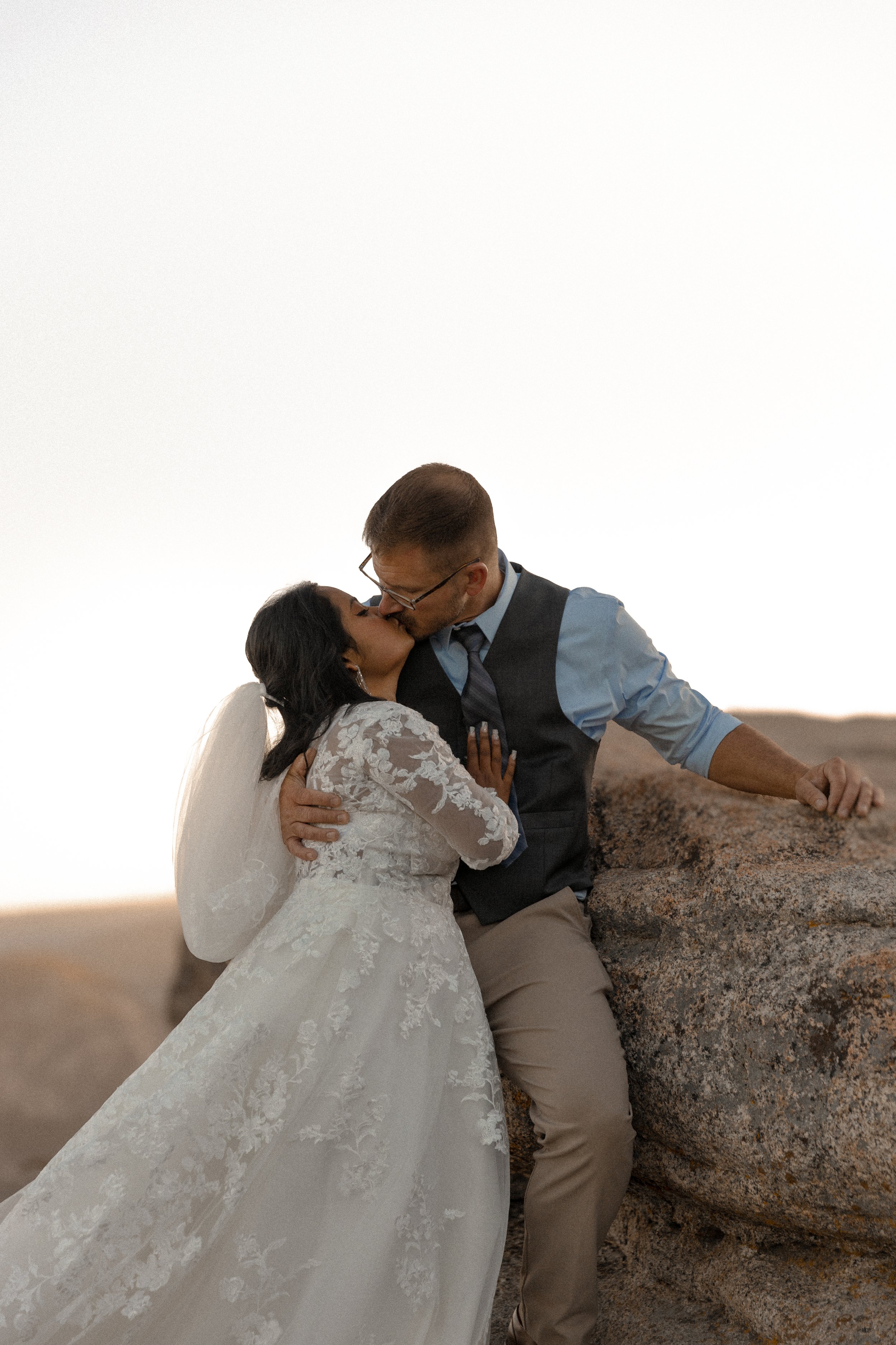 Bride and groom kissing on rocky landscape.