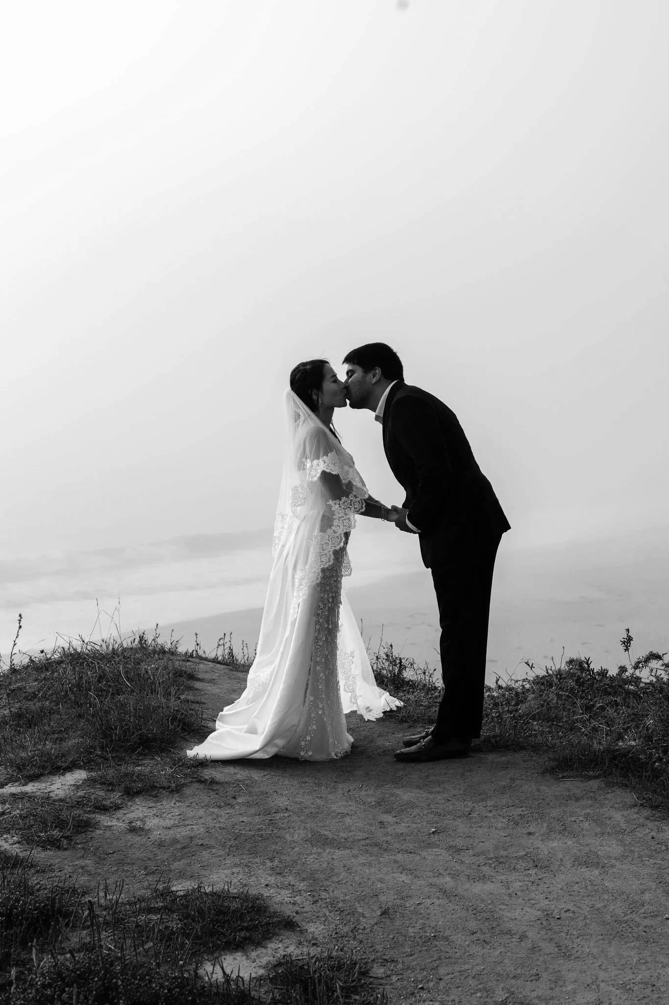 Wedding photography pricing inspiration at Half Moon Bay Ritz-Carlton with bride and groom kissing on coastal cliff overlooking ocean