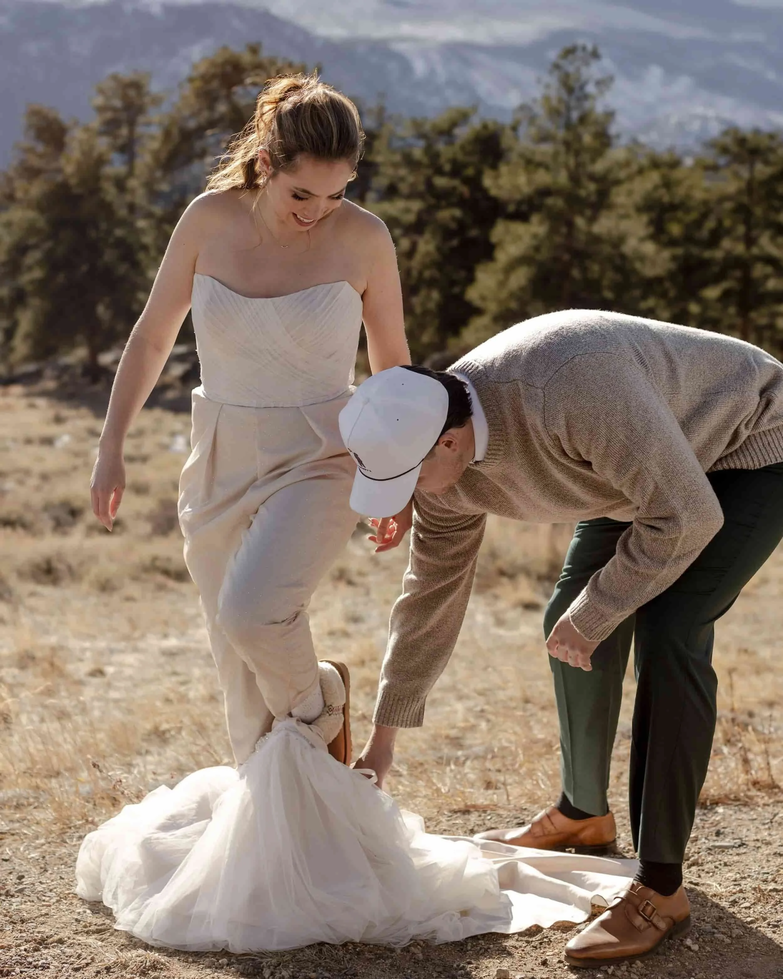 Bride adjusting dress with partner in a scenic mountain field at Rocky Mountain National Park, captured by a Colorado elopement photographer