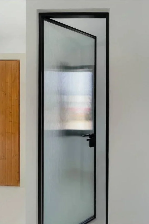 A black-framed glass door with a privacy film on the glass, installed in a white wall, with a wooden panel to the left.