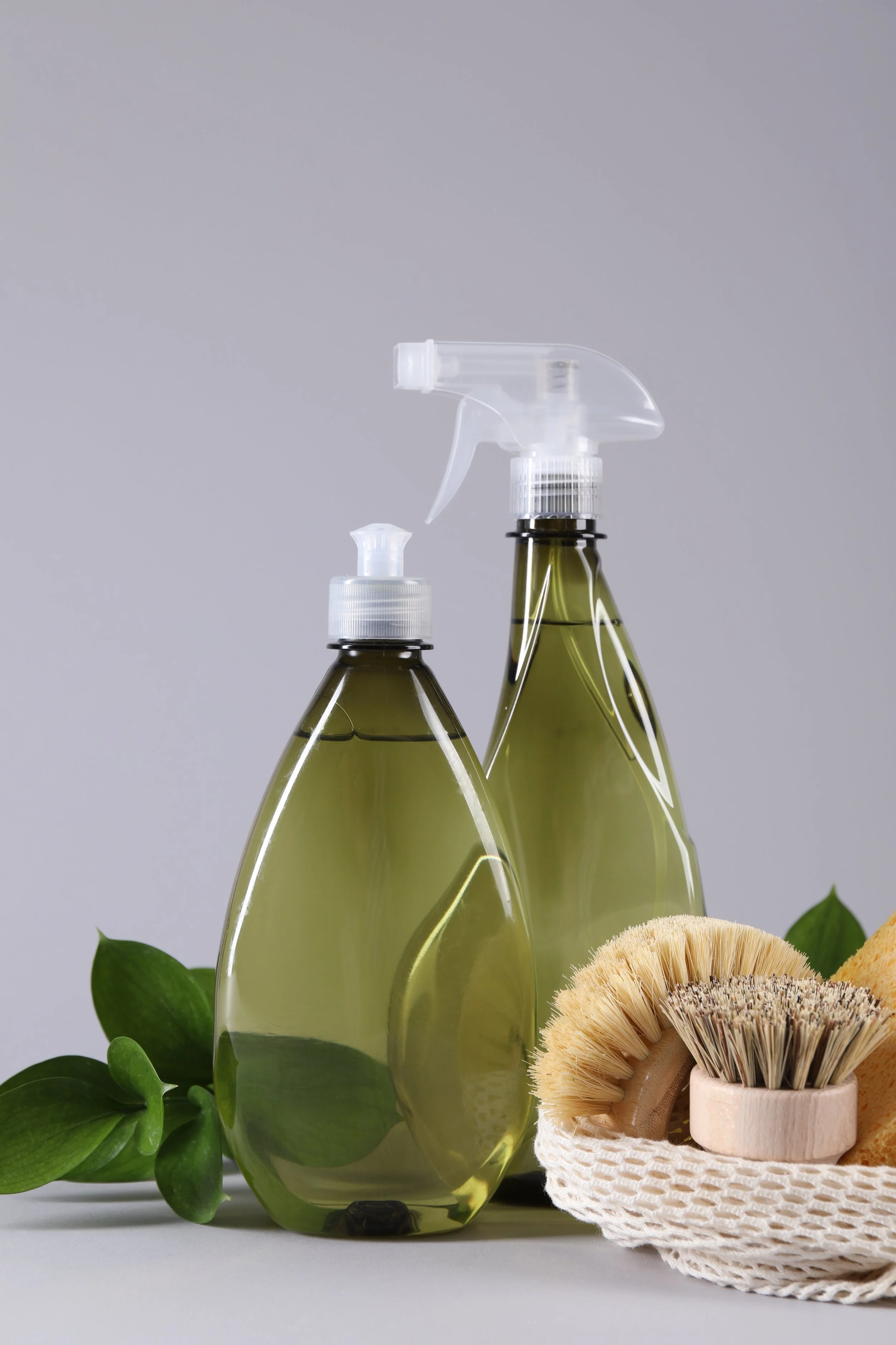 Eco-friendly cleaning products in spray bottles, surrounded by plant leaves and natural brushes, on a light background.