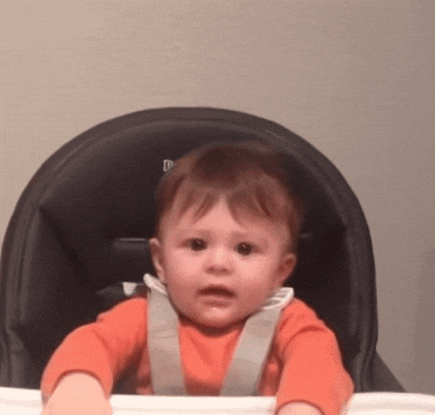 Baby in a high chair, wearing an orange top, raising his arms as if happily, but with a resigned look on their face. Supports article using an analogy of how small-medium businesses need to regularly maintain their branding regularly.