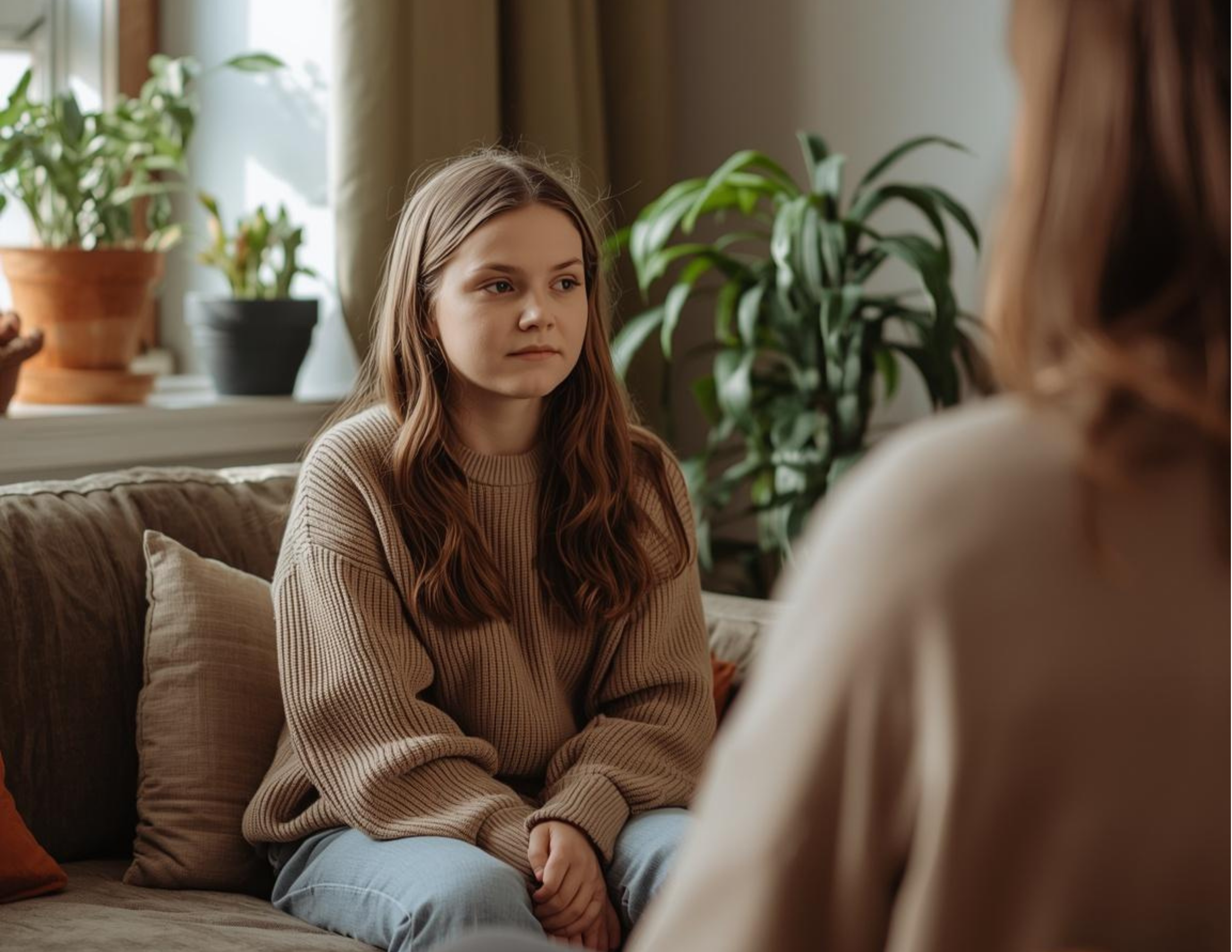 A teen girl in a brown shirt sits on a couch across from a therapist in a Tangible therapy office in Orem, Utah with a plant in the background