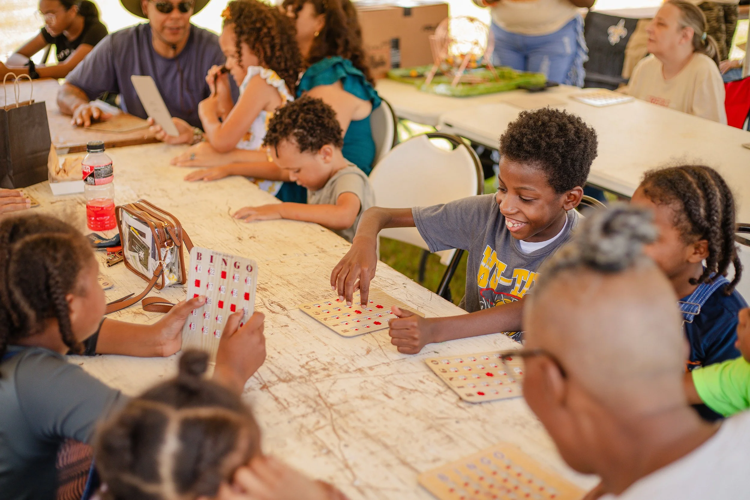 Children and adults playing bingo at a long table, with some children smiling and engaging in the game.