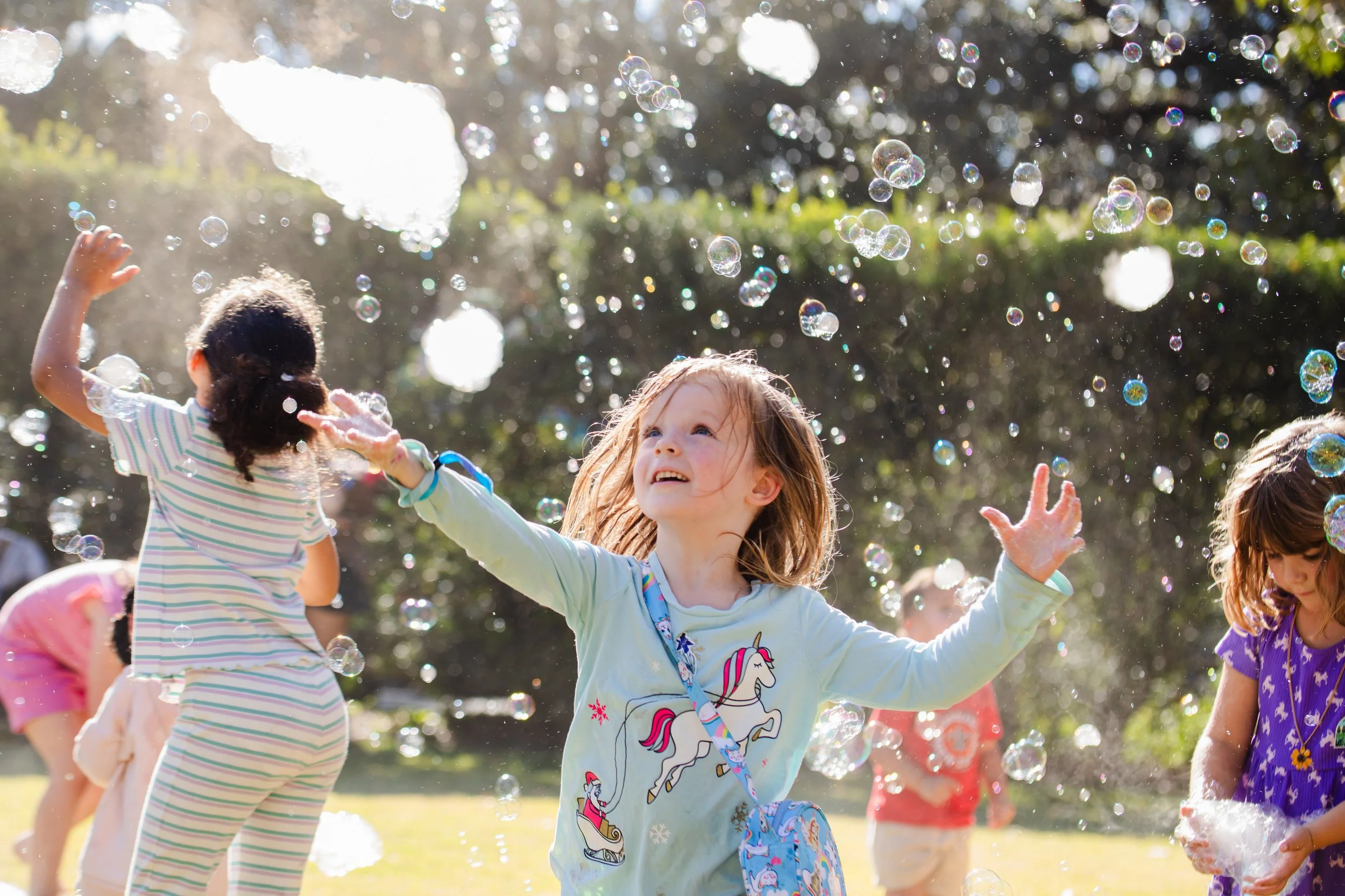 Children playing and having fun outdoors with bubbles on a sunny day.