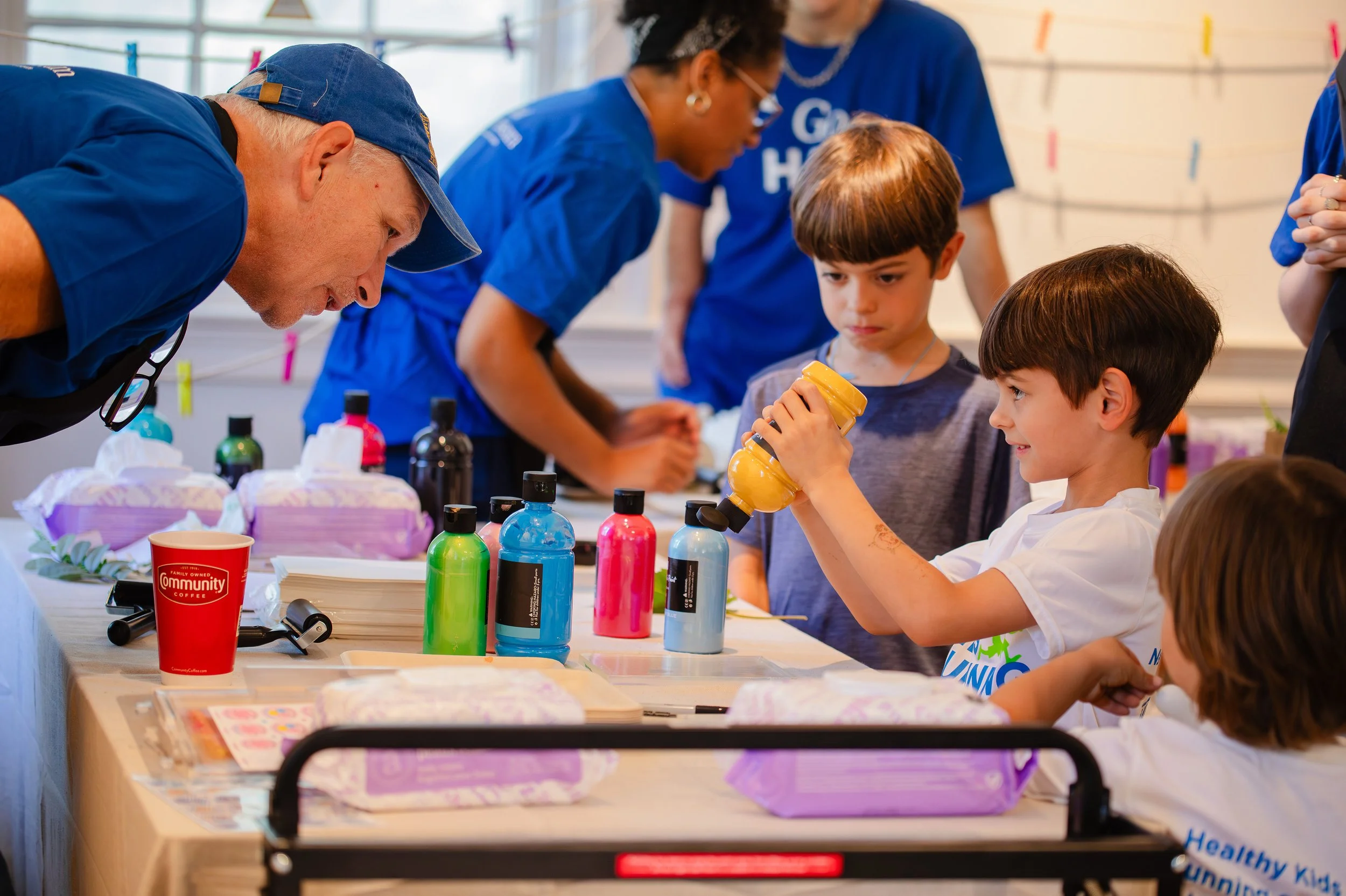 Children and adults at a table engaging in a science or arts activity, with colorful bottles and supplies on the table.