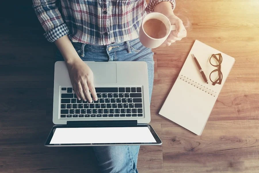 A top down view of a person typing on a laptop while holding a coffee cup. This could represent the ease of online career counseling in California. Learn more about online career counseling in San Francisco, CA by contacting a career counselor.