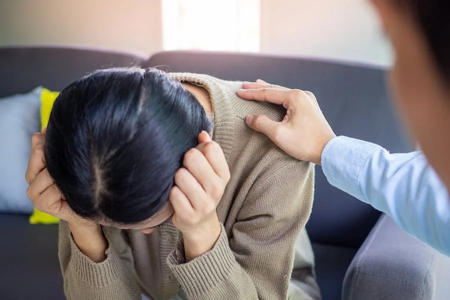 Image of a person with their head down and looking upset while another person puts a hand on their shoulder. This image depicts how someone in counseling for life transitions in San Francisco, CA may look like. | 94115 | 94131 | 94158