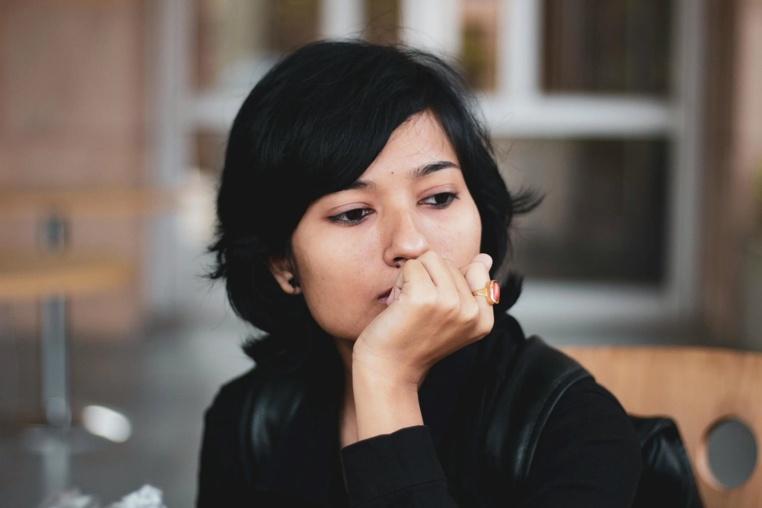 Adult sitting quietly in soft natural light, reflecting inward, representing chronic bracing and emotional patterns associated with Complex PTSD