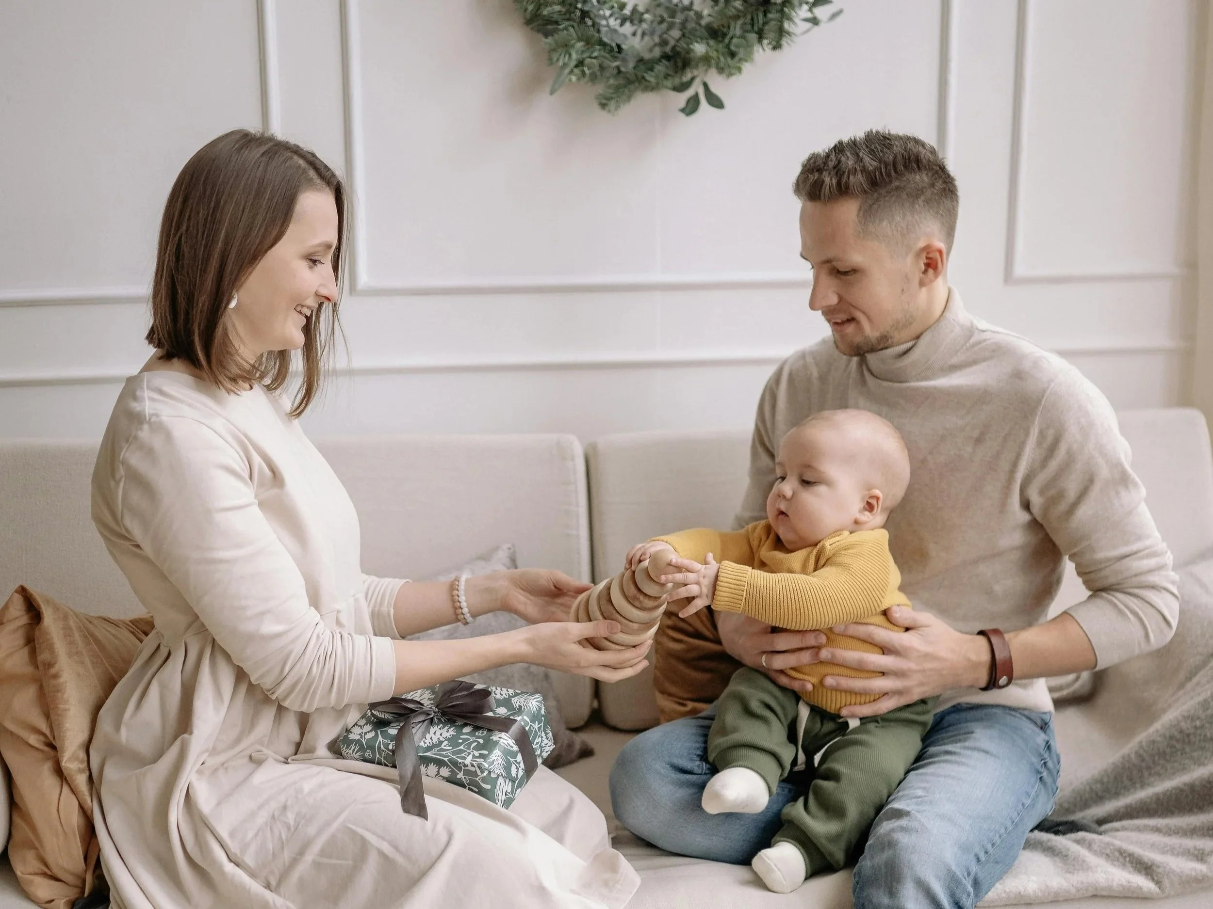 A smiling couple sitting on a couch with their baby, sharing a quiet moment together — symbolizing connection and support for relationships after having a child.