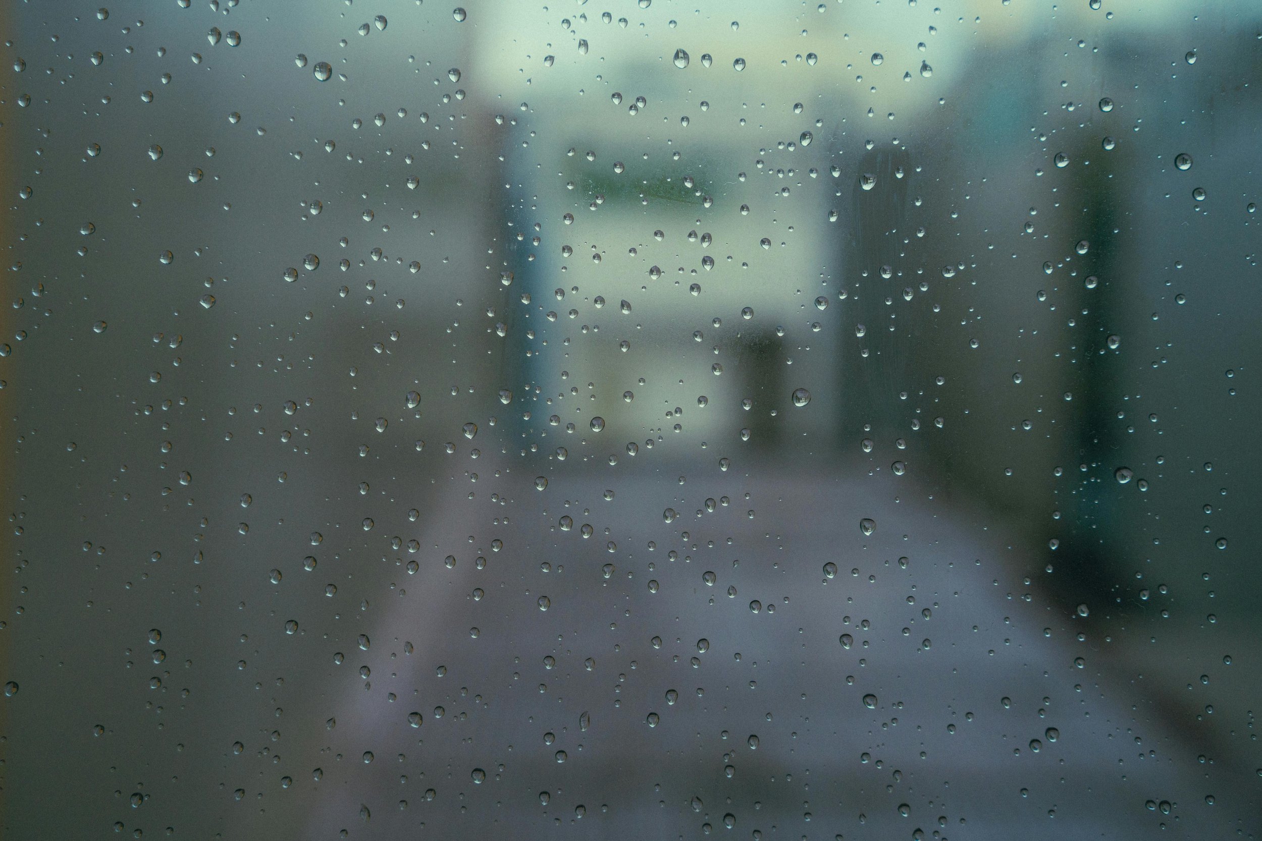Soft rain on a window in a calm indoor space, representing reflection and emotional processing after a community tragedy.