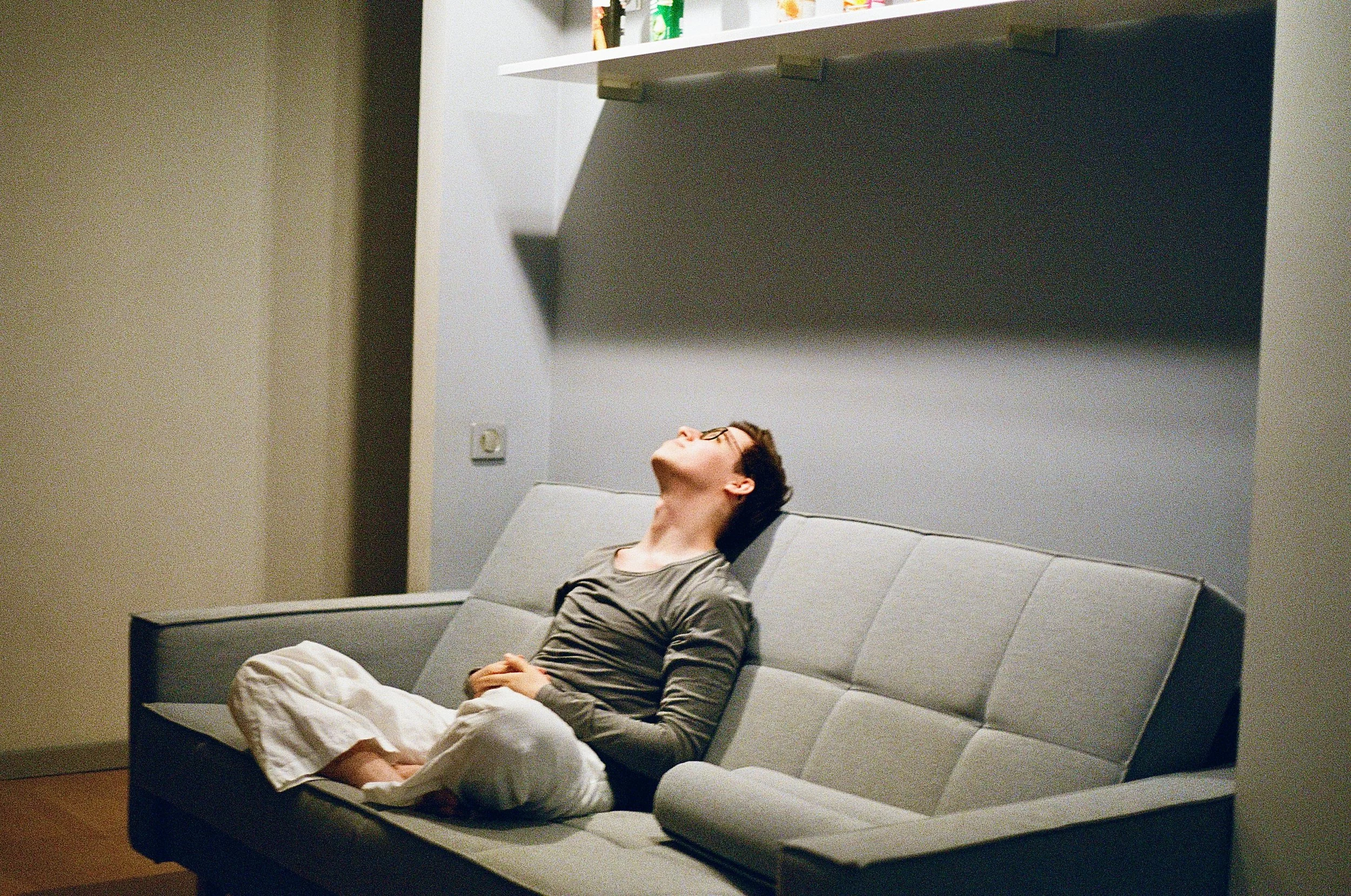 Person sitting quietly on a couch appearing physically tense and emotionally restless while trying to relax at home