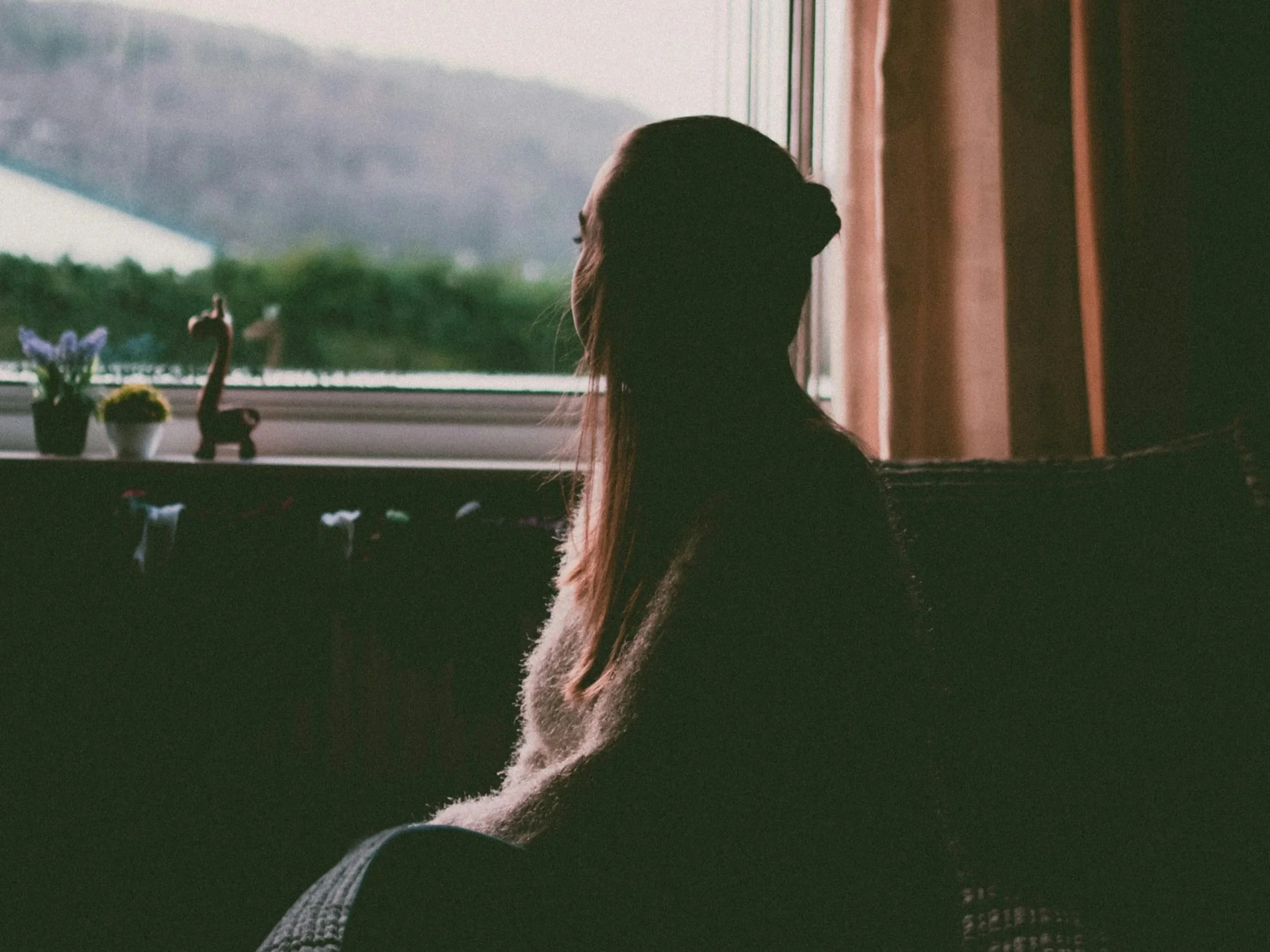 Person sitting thoughtfully at home, representing avoidance patterns and gentle support in online anxiety therapy.