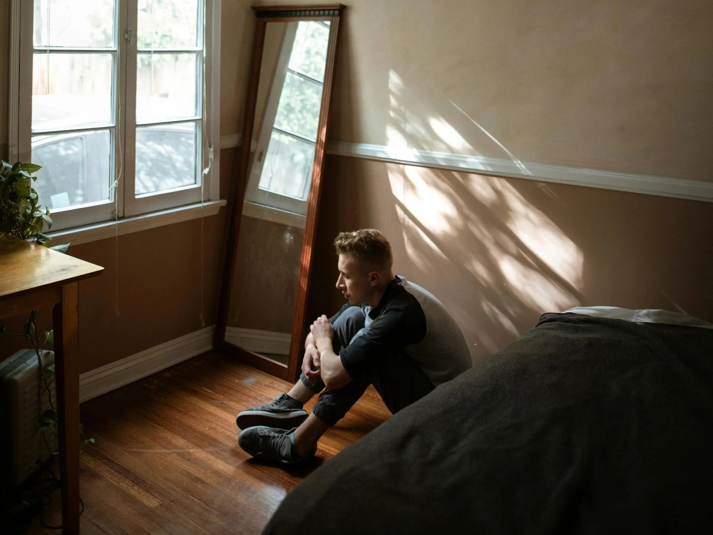 Man sitting quietly in natural light, reflecting on unspoken emotional weight.