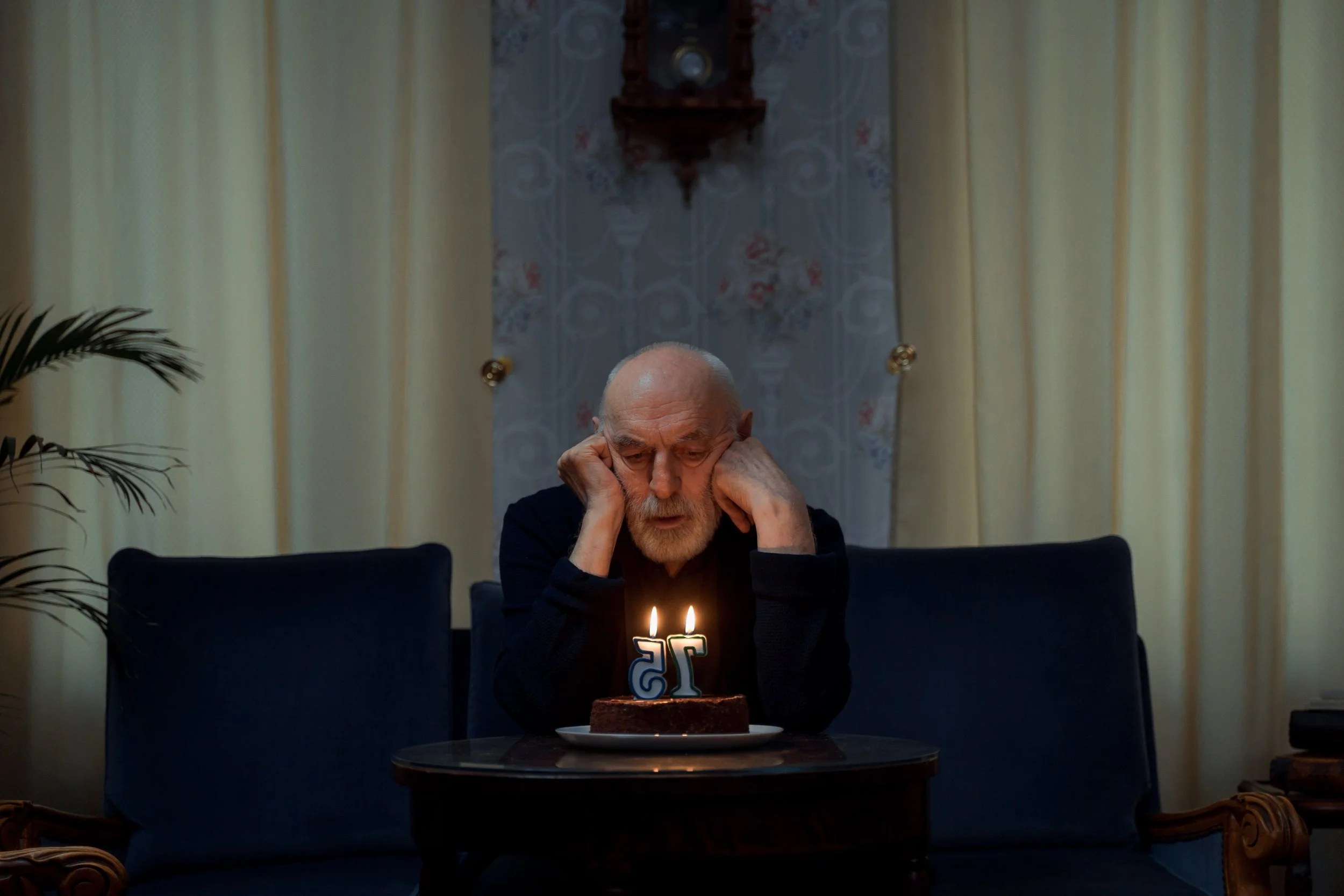 Person reflecting quietly beside a birthday cake while experiencing complicated birthday emotions