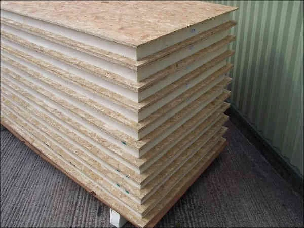 Stack of engineered wood or plywood sheets leaning against a green wall in an indoor setting.