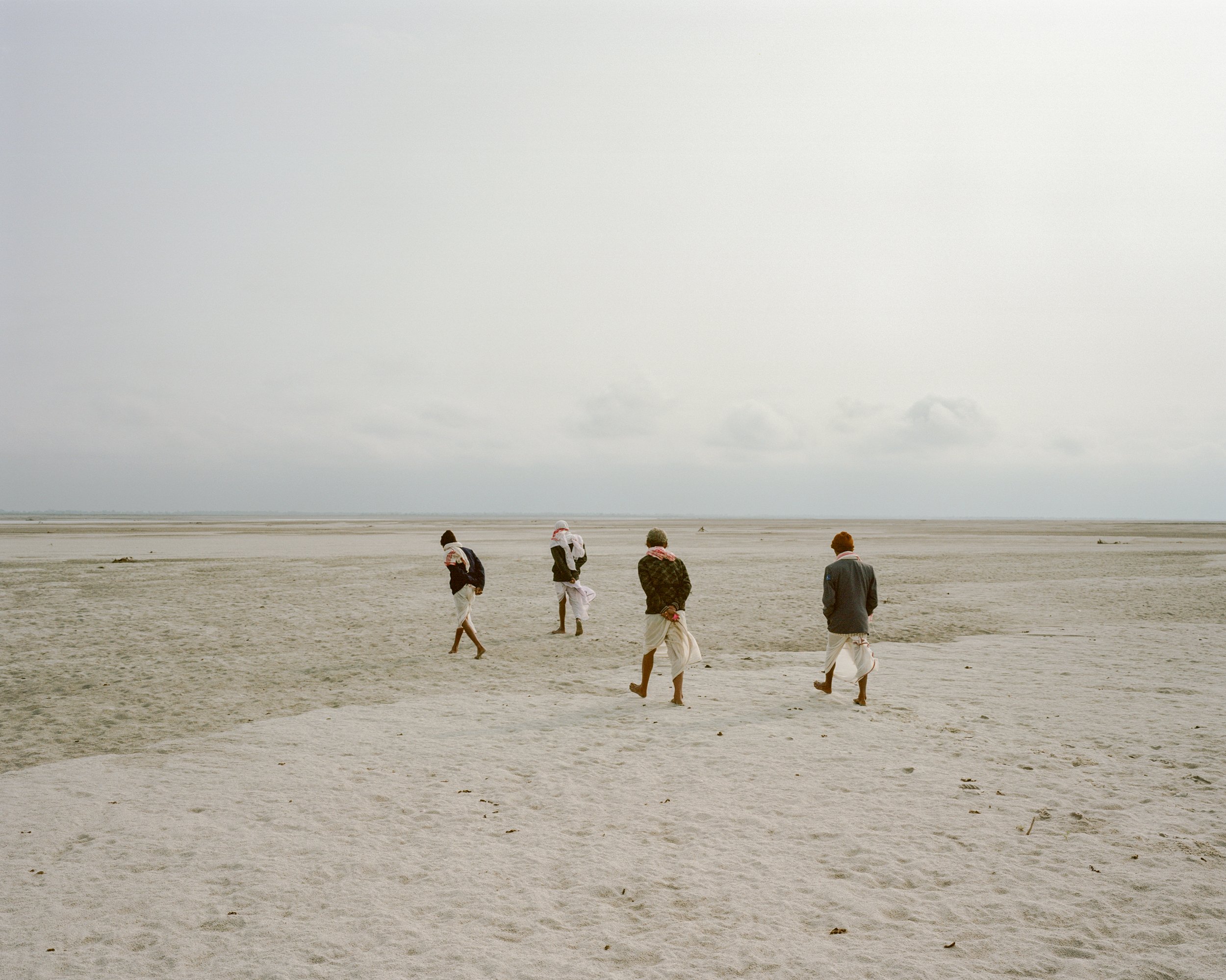   Elders walking on the riverbed of Brahmaputra after praying for gods of the river.   Salmora Chapori, Majuli, India — 2021  