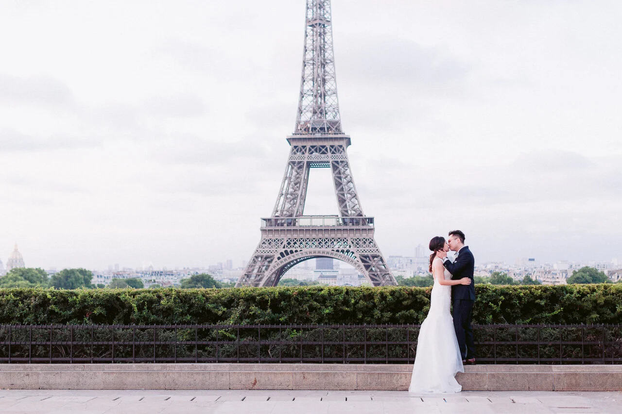 A bride and groom kissing in front of the Eiffel Tower in Paris, France, on their wedding day.