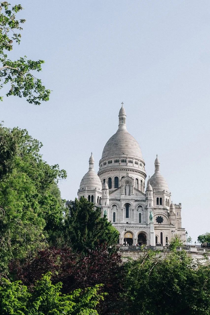 Sacré-Cœur Basilica glowing in soft golden morning light through the trees of the surrounding gardens