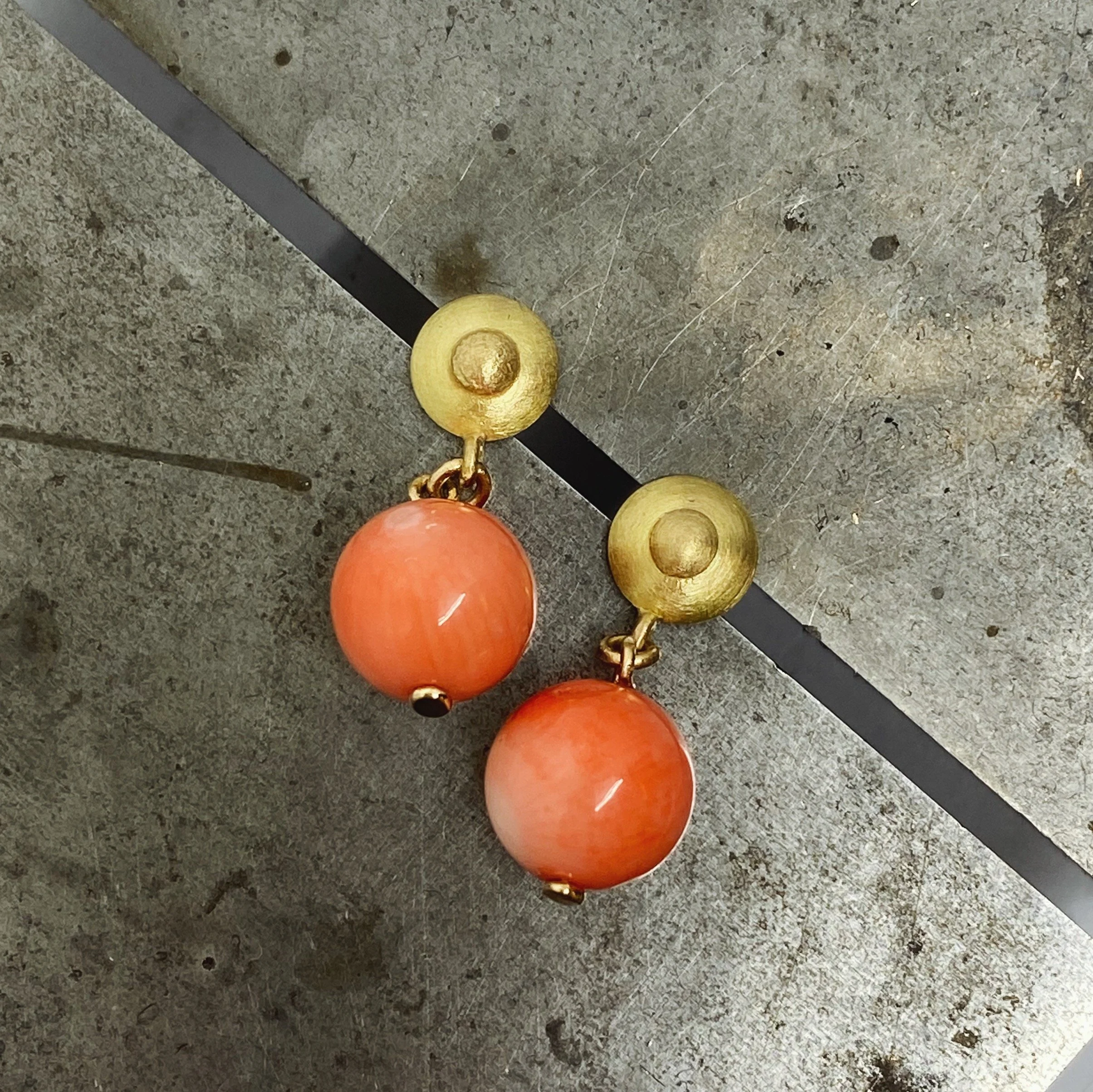 Ett par guldörhängen i antik stil med korallkulor på en metallisk yta.