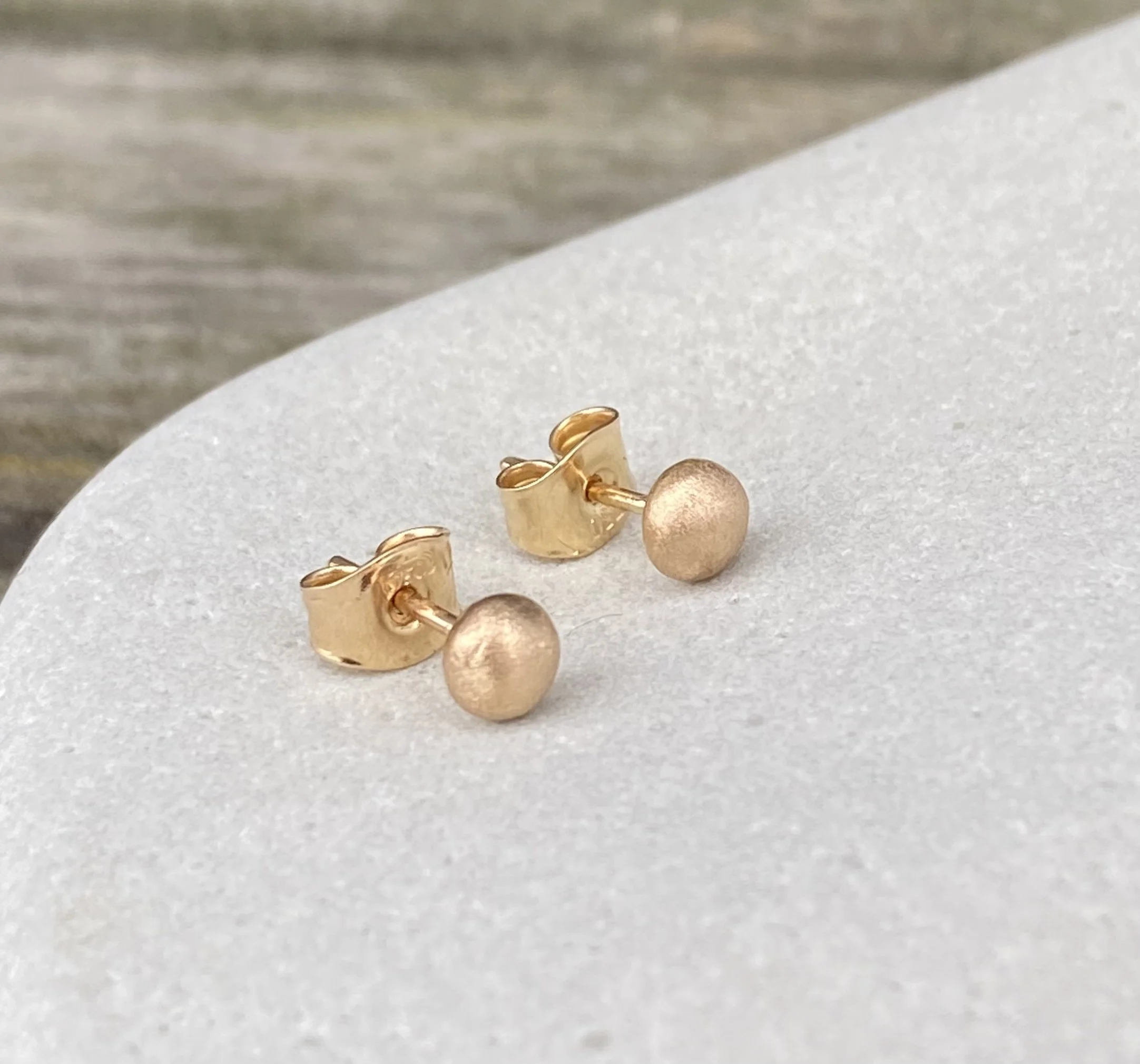 Ett par örhängen i guld, små guldklimpar på stift, på en vit sten.