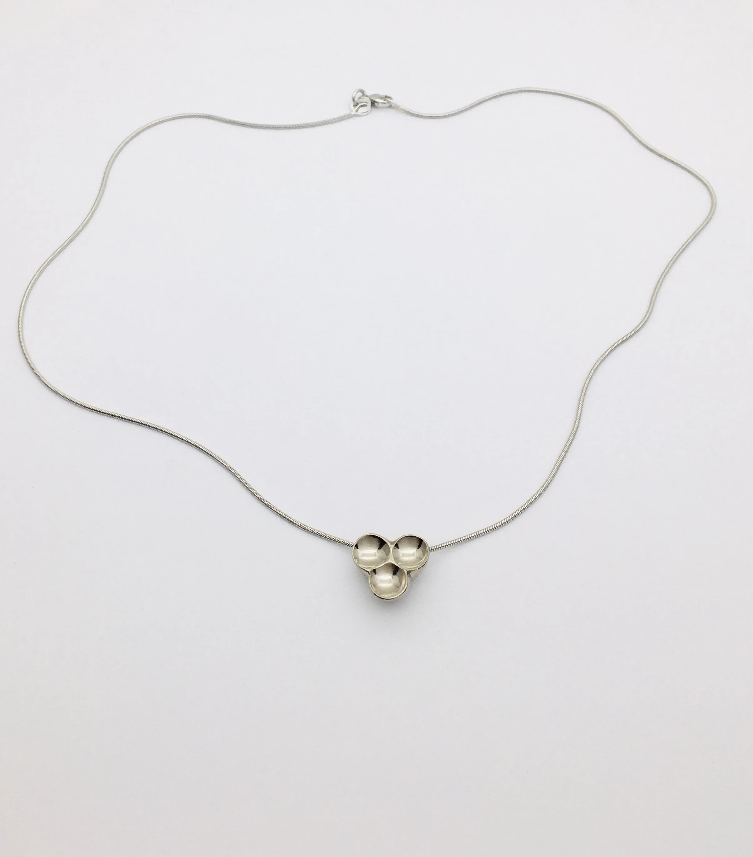 Halsband i vitguld med ett hänge med tre sammankopplade sfärer mot vit bakgrund.