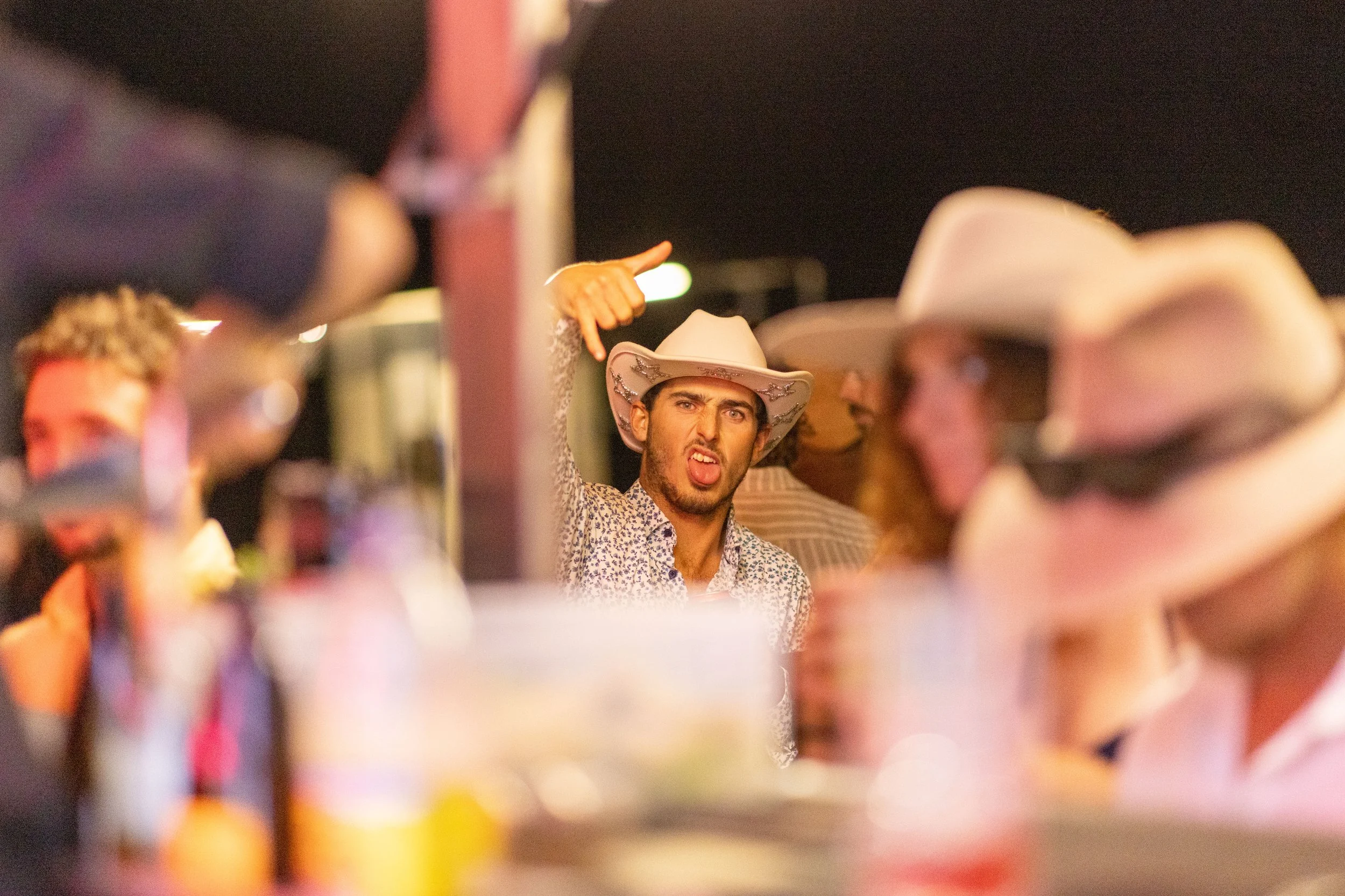 Young man wearing a cowboy hat making a sassy face at a party or bar, surrounded by others also wearing cowboy hats. Kalbarri Gala