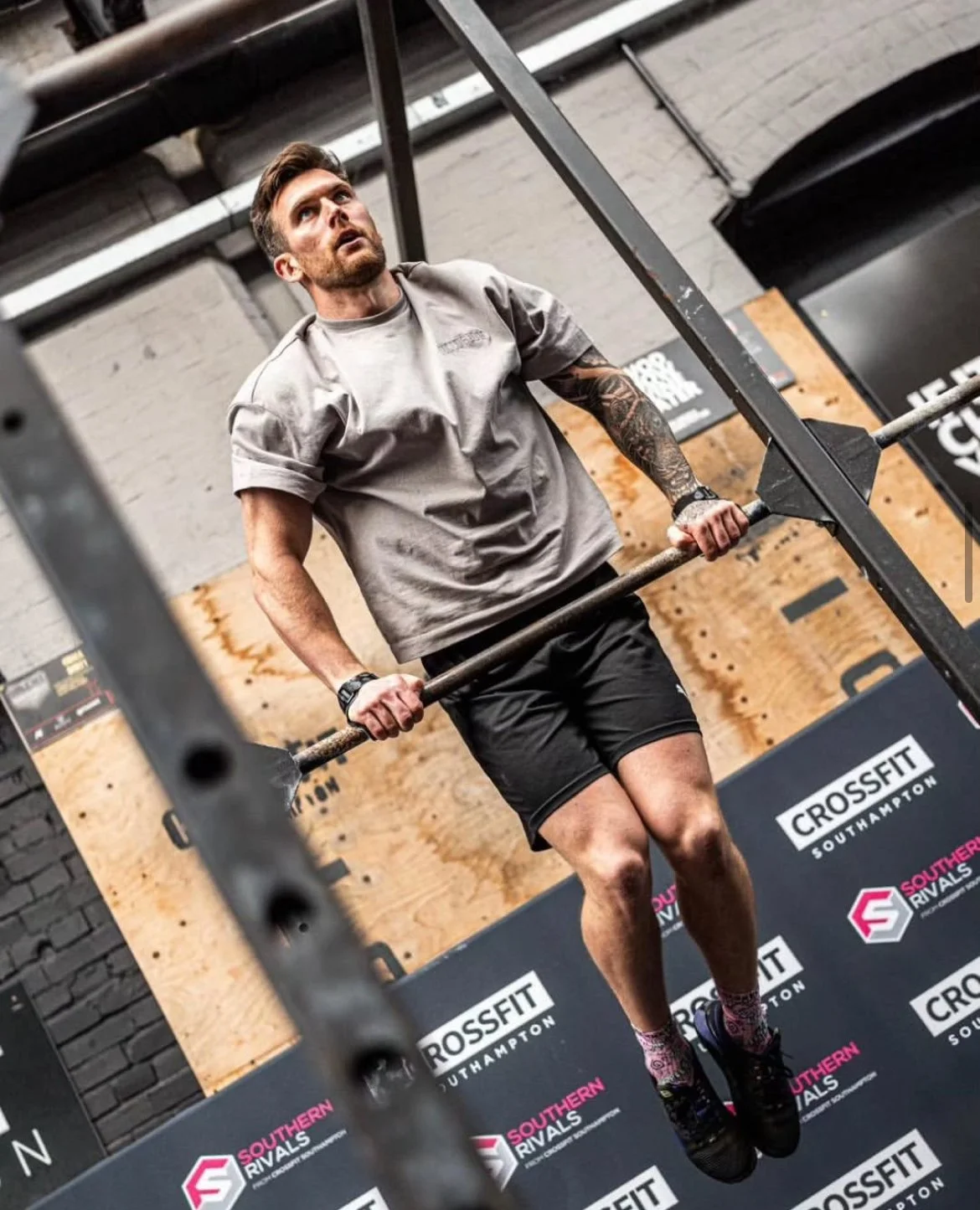 Man performing a pull-up at Crossfit gym, holding a barbell with both hands, with Crossfit Southhampton and Southern Rivals banners in background.