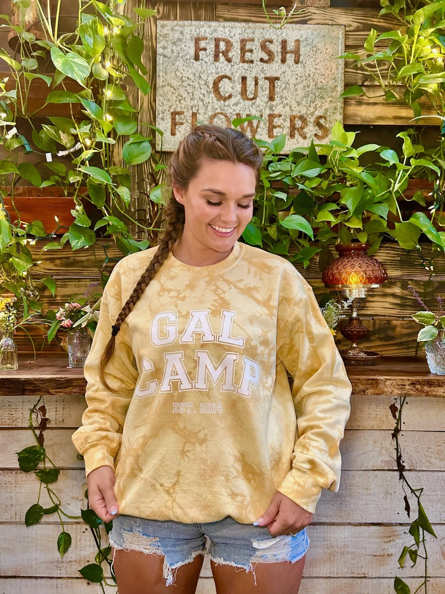 yellow varsity letter hand dyed, tie dye sweater. young lady in braids in standing in front of a wall with hanging plants