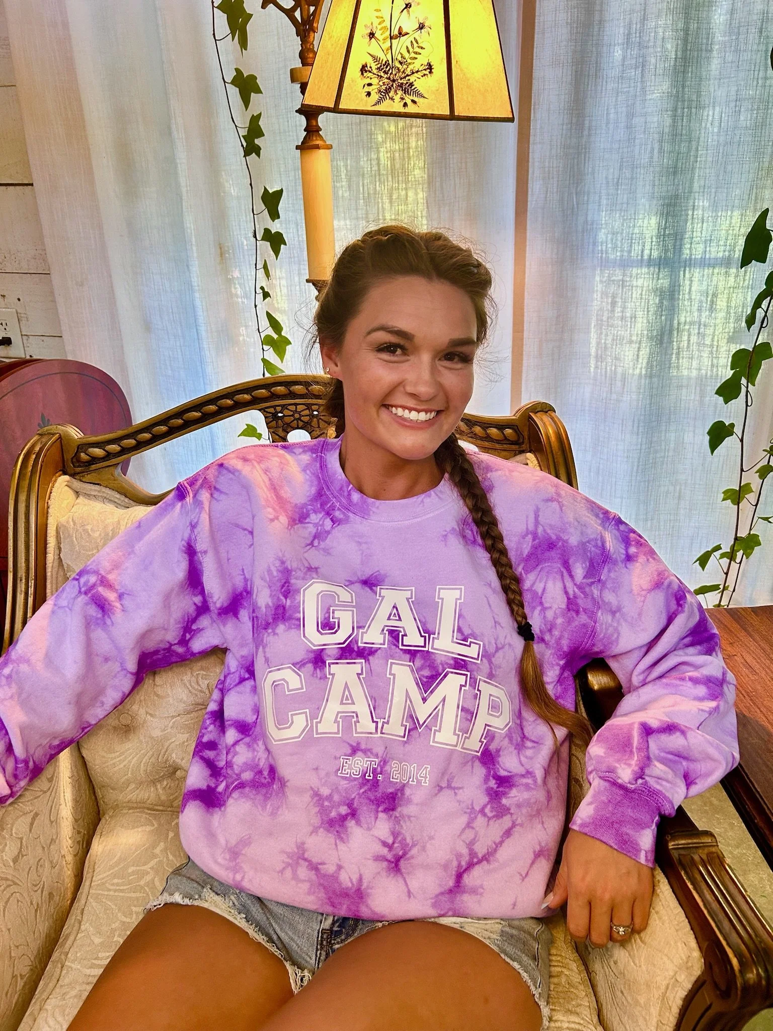 varsity letter hand dyed, tie dyed sweater in purple color. young lady with braids sitting in a chair