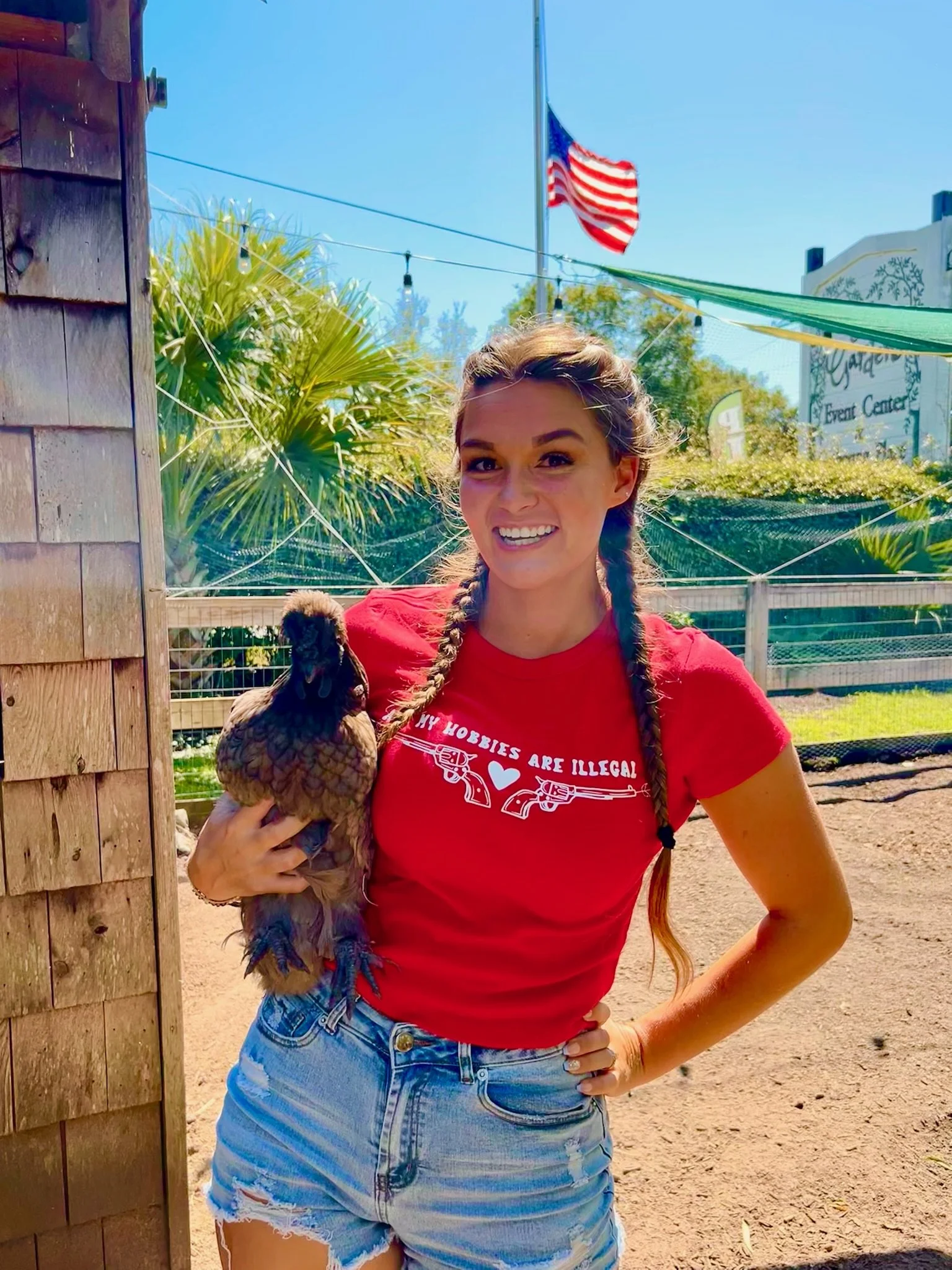 young lady with braids holding a chicken wearing a red shirt with the American flag in the background