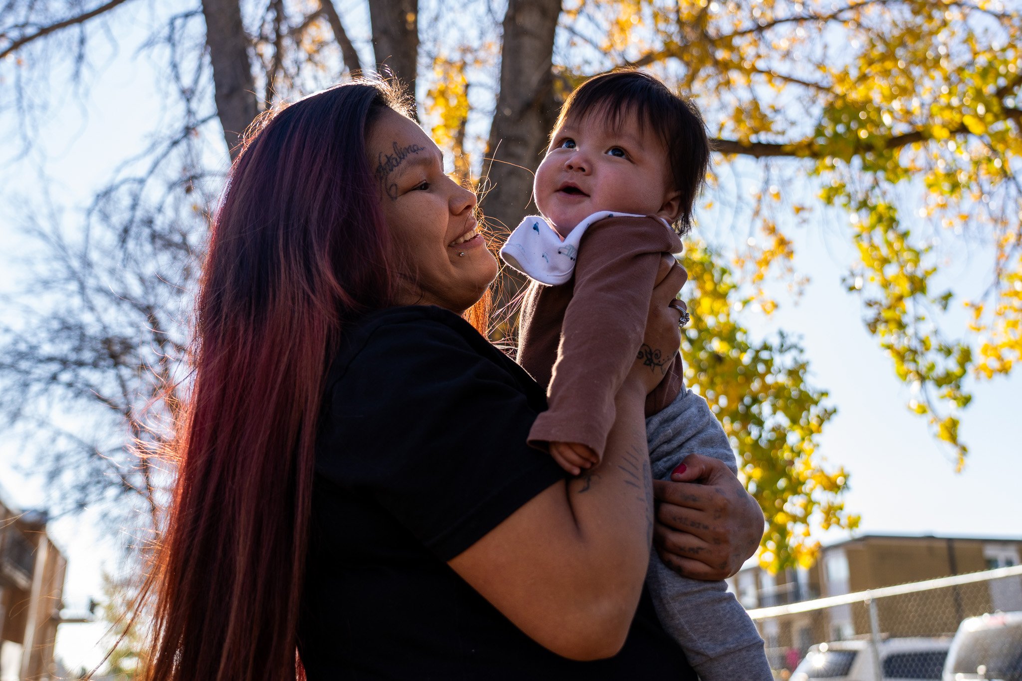 Two people riding bicycles along a riverside path with city buildings in the background, one woman and one man, both wearing helmets.