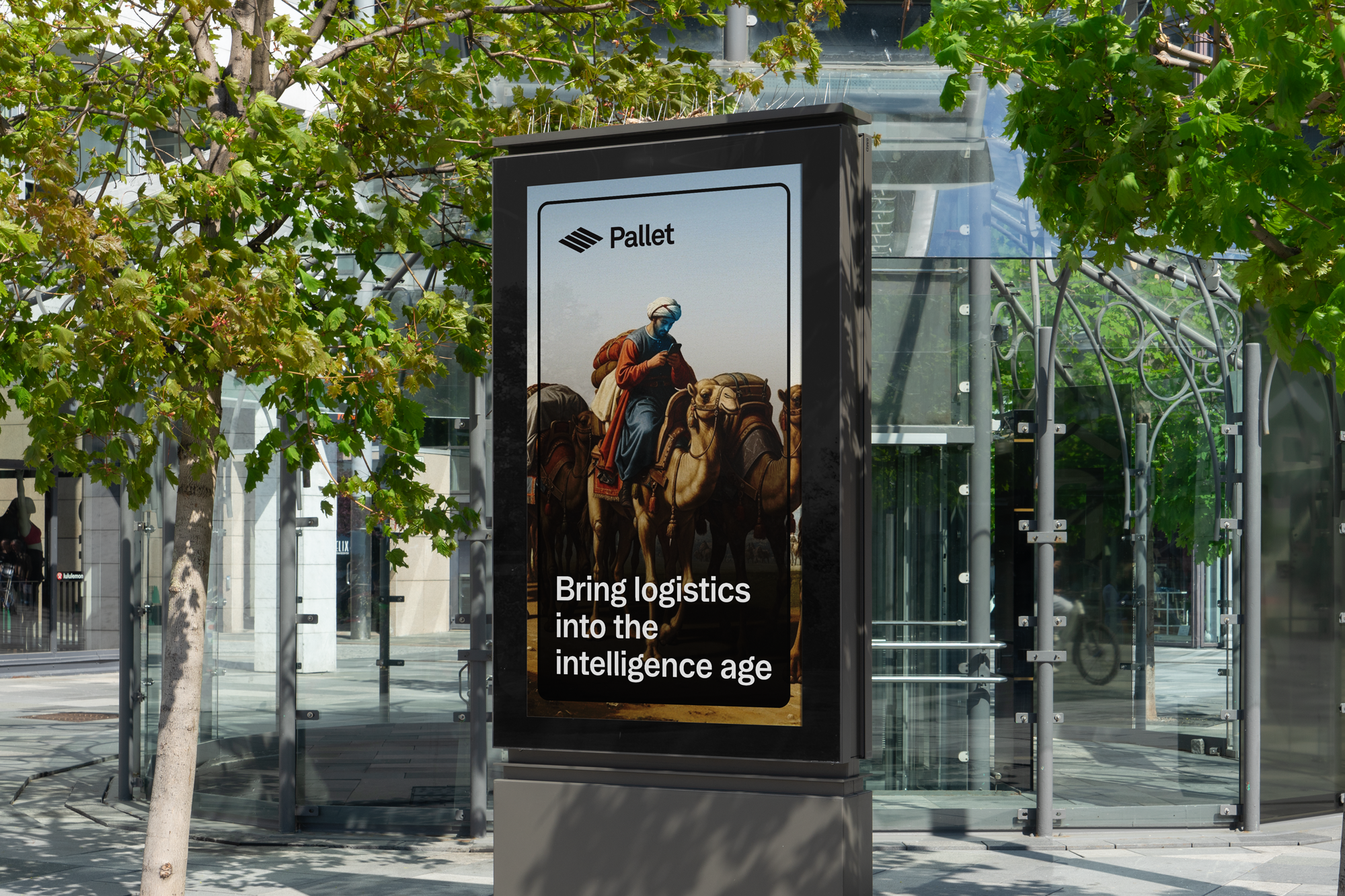 Outdoor advertisement billboard with a historical painting of a man riding a camel and looking at a mobile device, with the text 'Bring logistics into the intelligence age'; the billboard is in front of a modern glass bus stop with greenery and trees around.
