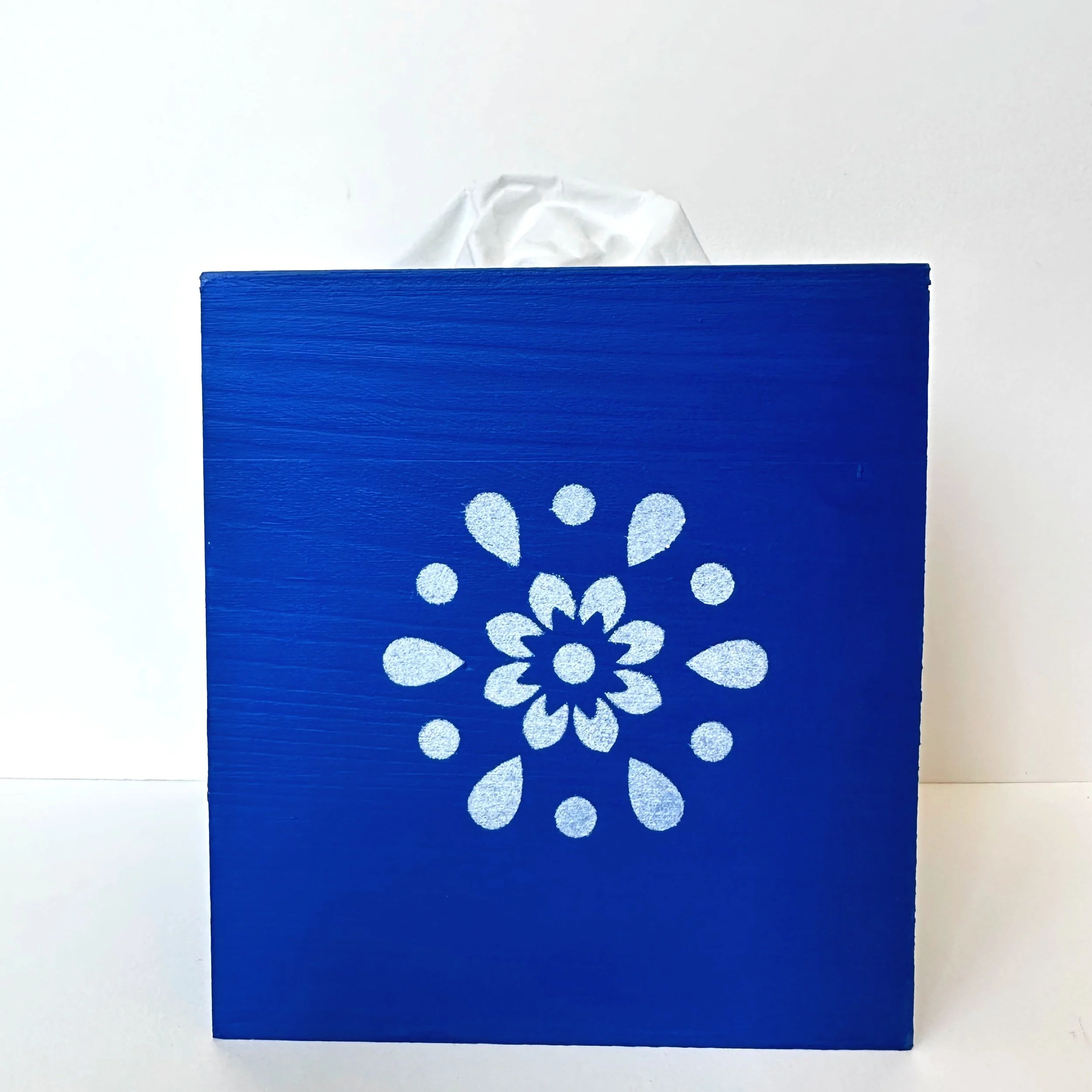 Blue tissue box with white floral pattern on front, with tissue paper protruding from the top.