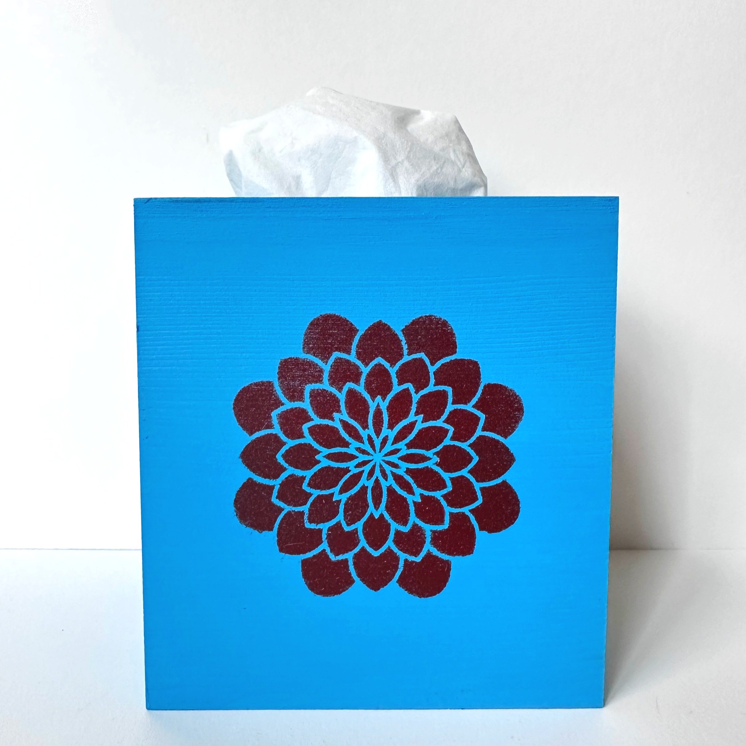 Blue tissue box with a dark red floral design, tissue protruding from the top, against a white background.