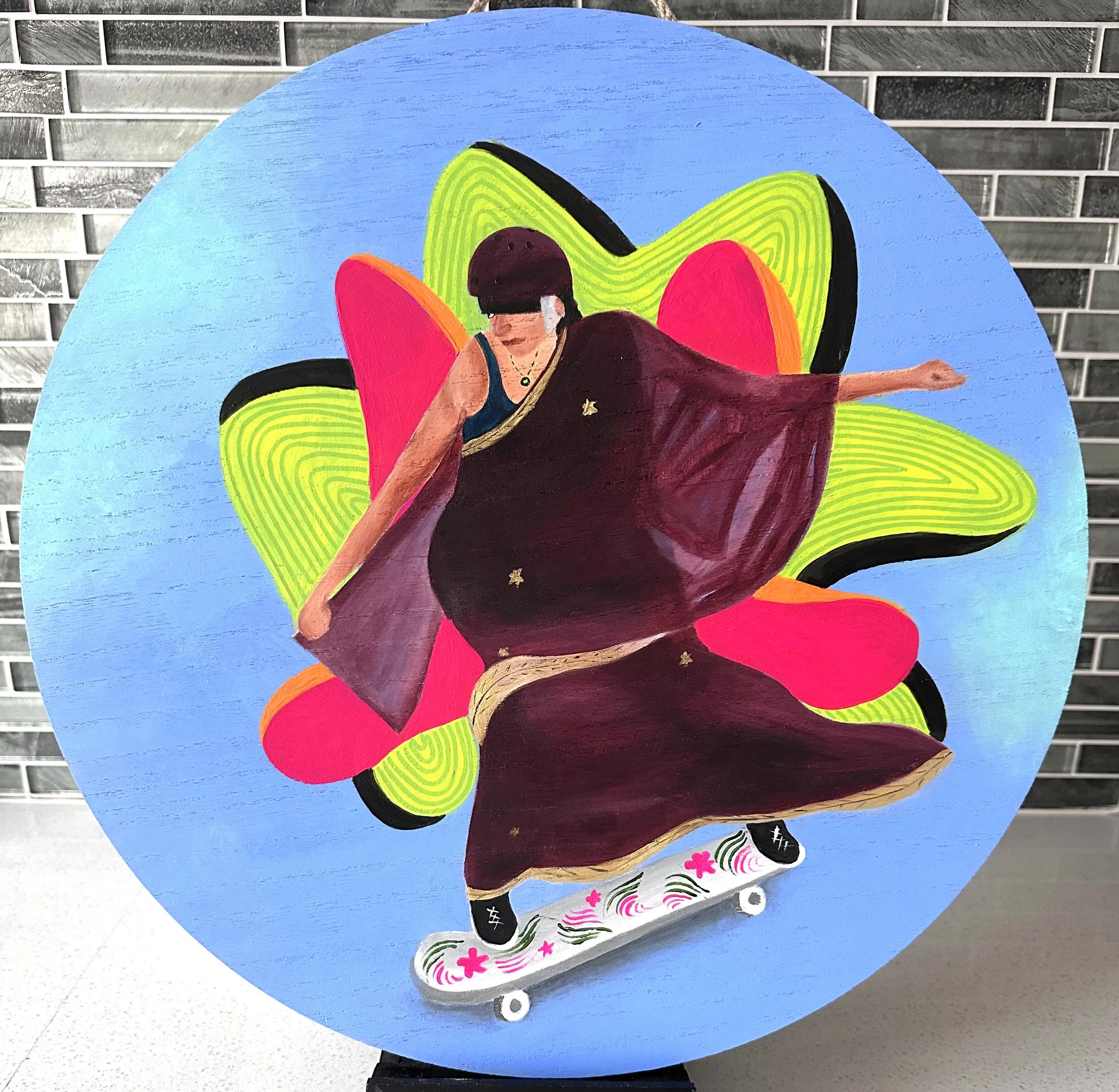 Colorful painting on a blue circular background depicting a woman skateboarding. The woman is dressed in a long, flowing burgundy dress and black shoes. Behind her is a vibrant, abstract flower made of bright pink, orange, and green shapes.