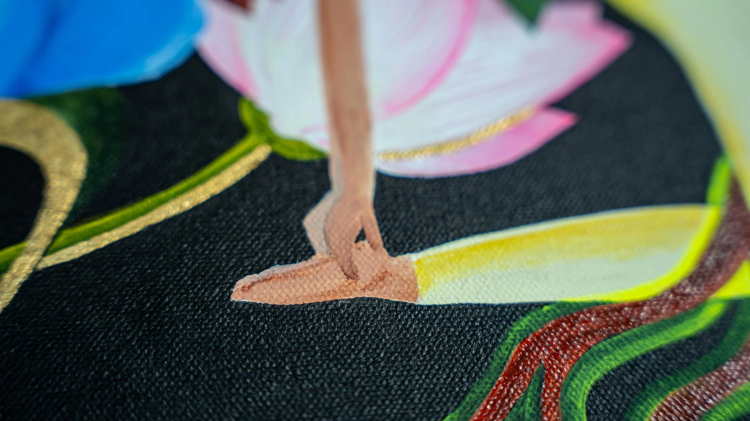 Close-up of a colorful embroidered fabric featuring a pink flower, yellow and green leaves, and part of a graceful leg and foot, with black background and gold accents.