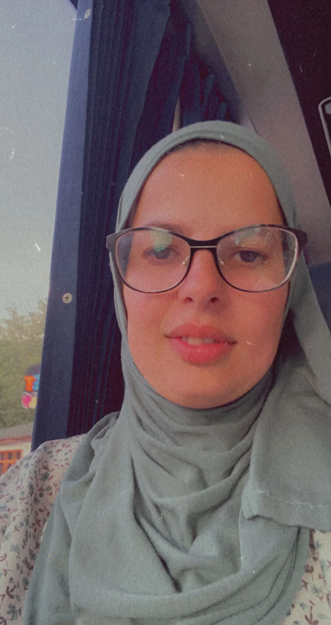 A woman with glasses and a hijab taking a selfie inside a bus or vehicle.