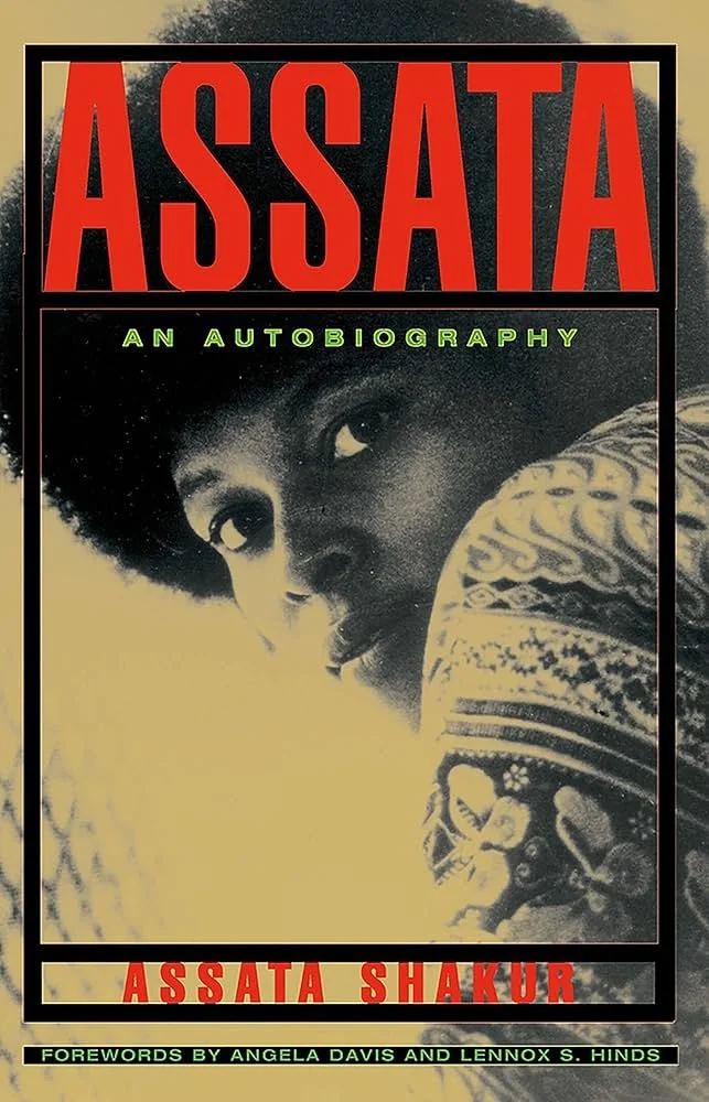 Book cover of 'Assata: An Autobiography' by Assata Shakur, featuring a black and white portrait of a woman with an afro hairstyle looking over her shoulder, with colorful clothing visible. The title is in large red letters at the top, with the author's name in red at the bottom and a note about forewords at the bottom.
