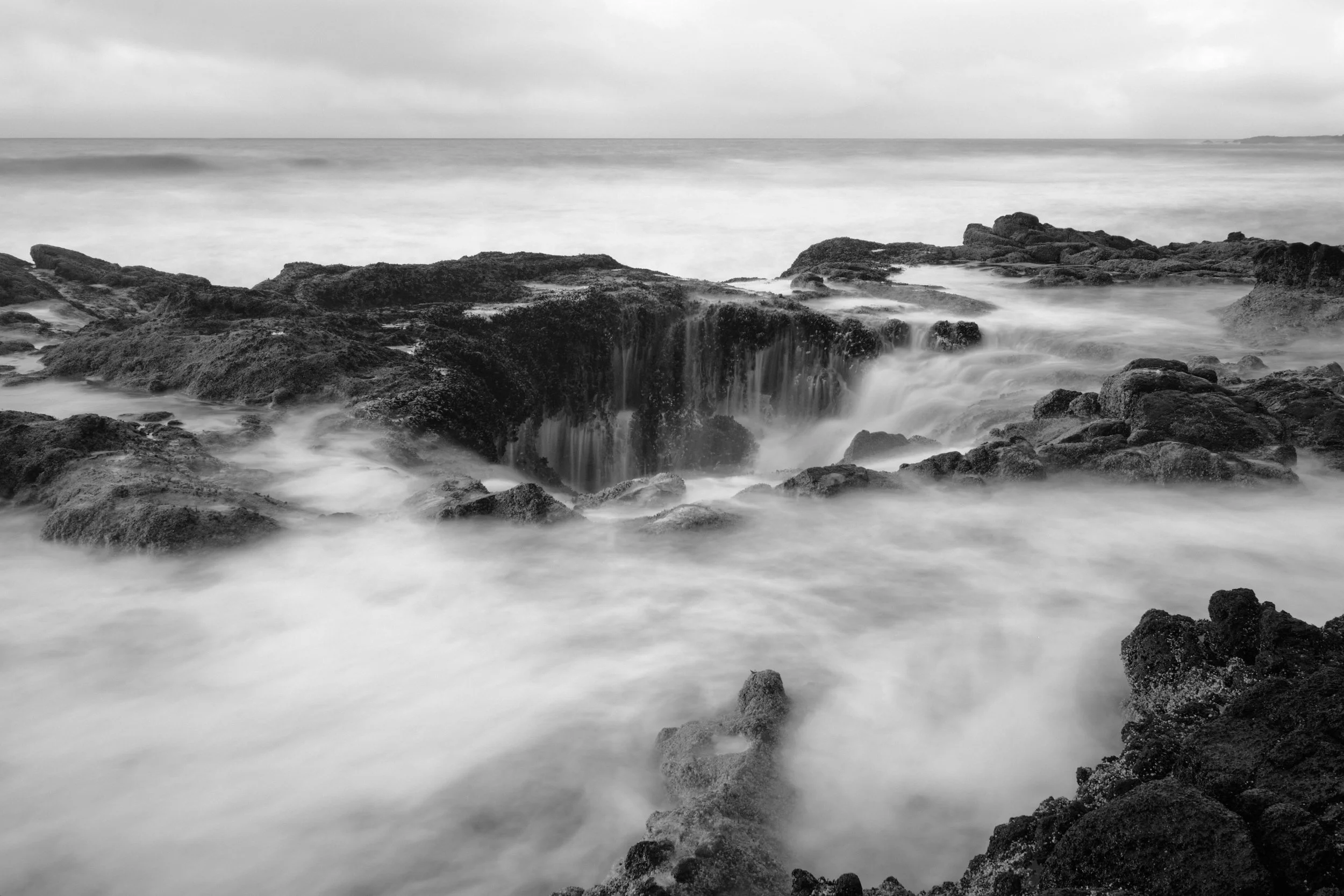 Thor's Well, a hole in the rock on an Oregon beach has misty water flowing into it after a wave crashed onto the coast.