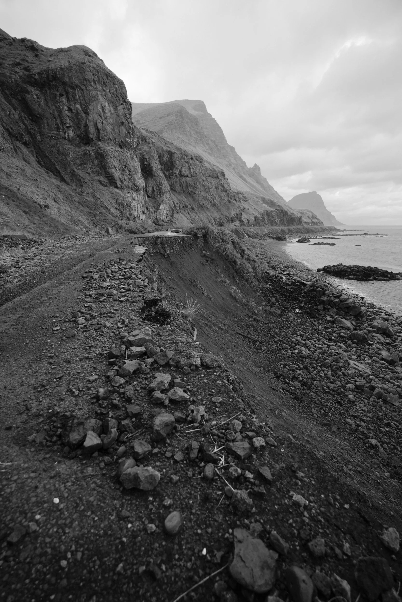 Tall mountains stand before an abandon road that is crumbling into the sea in the Iceland Westfjords.